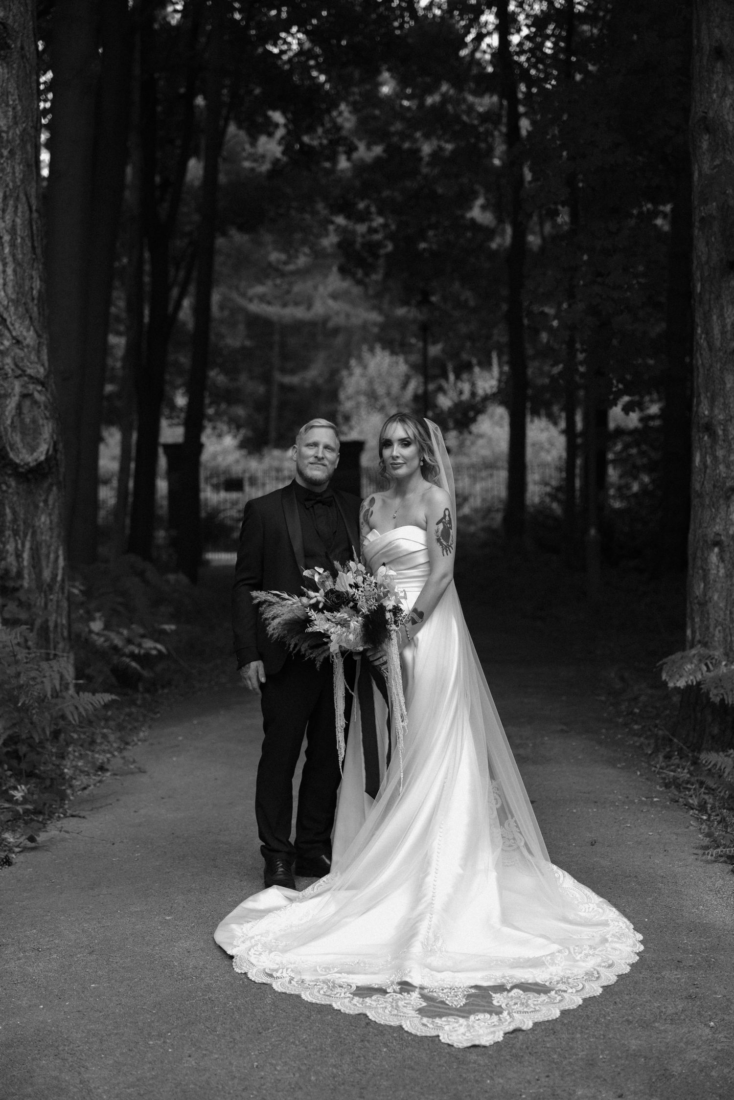 Black and white wedding photos on tree-lined path showing elegant bridal dress.