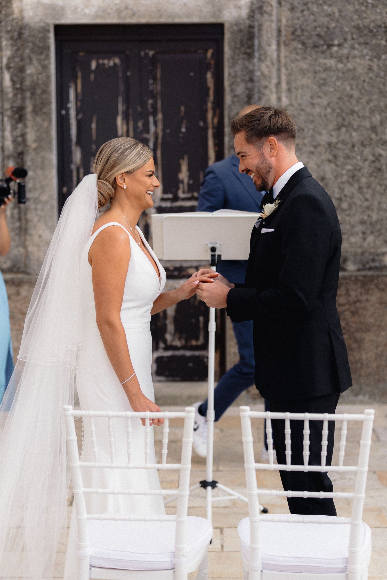 Wedding couple interacting in front of white Chiavari chairs at an outdoor venue.