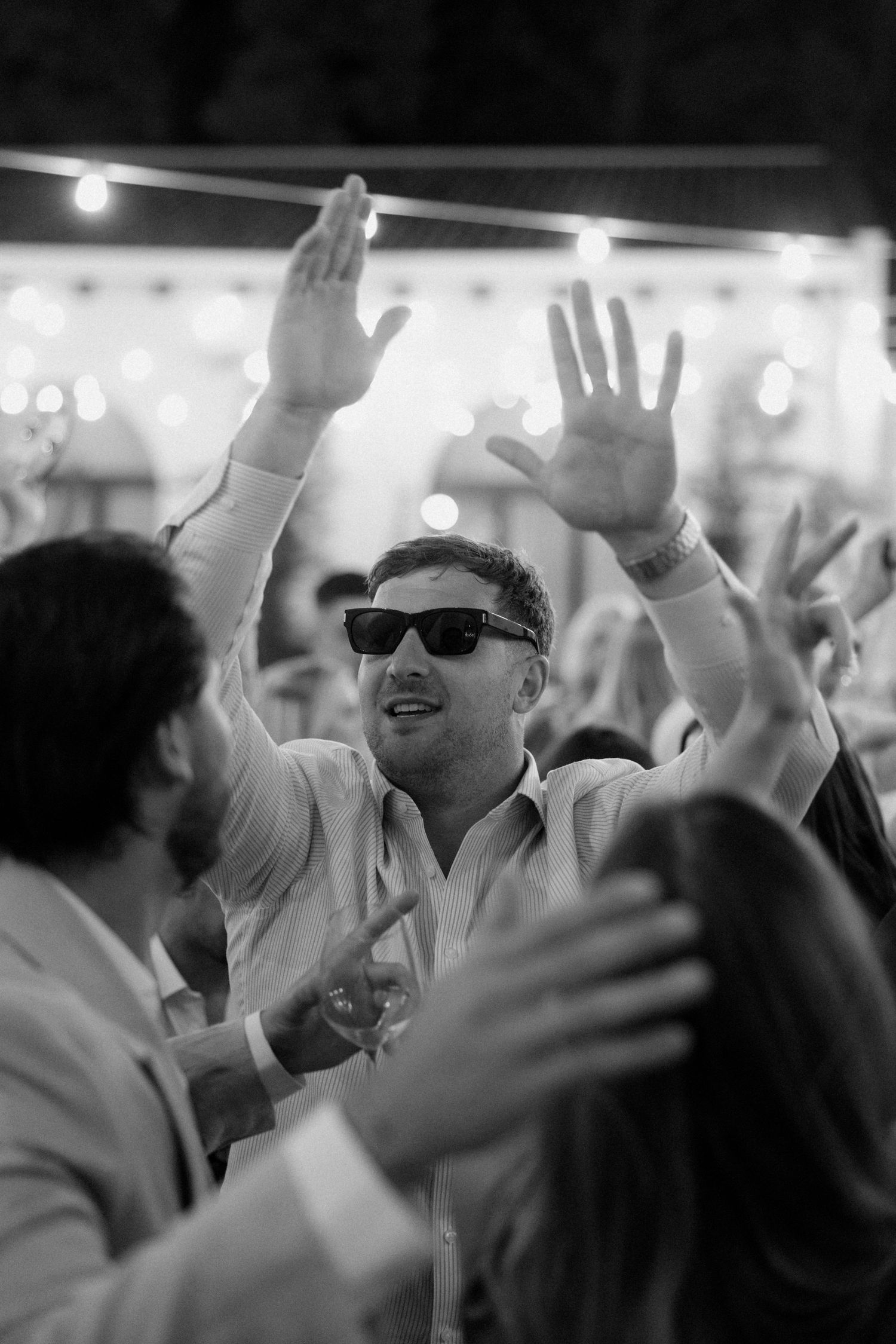 Wedding guests dancing with raised hands at a lively reception party.