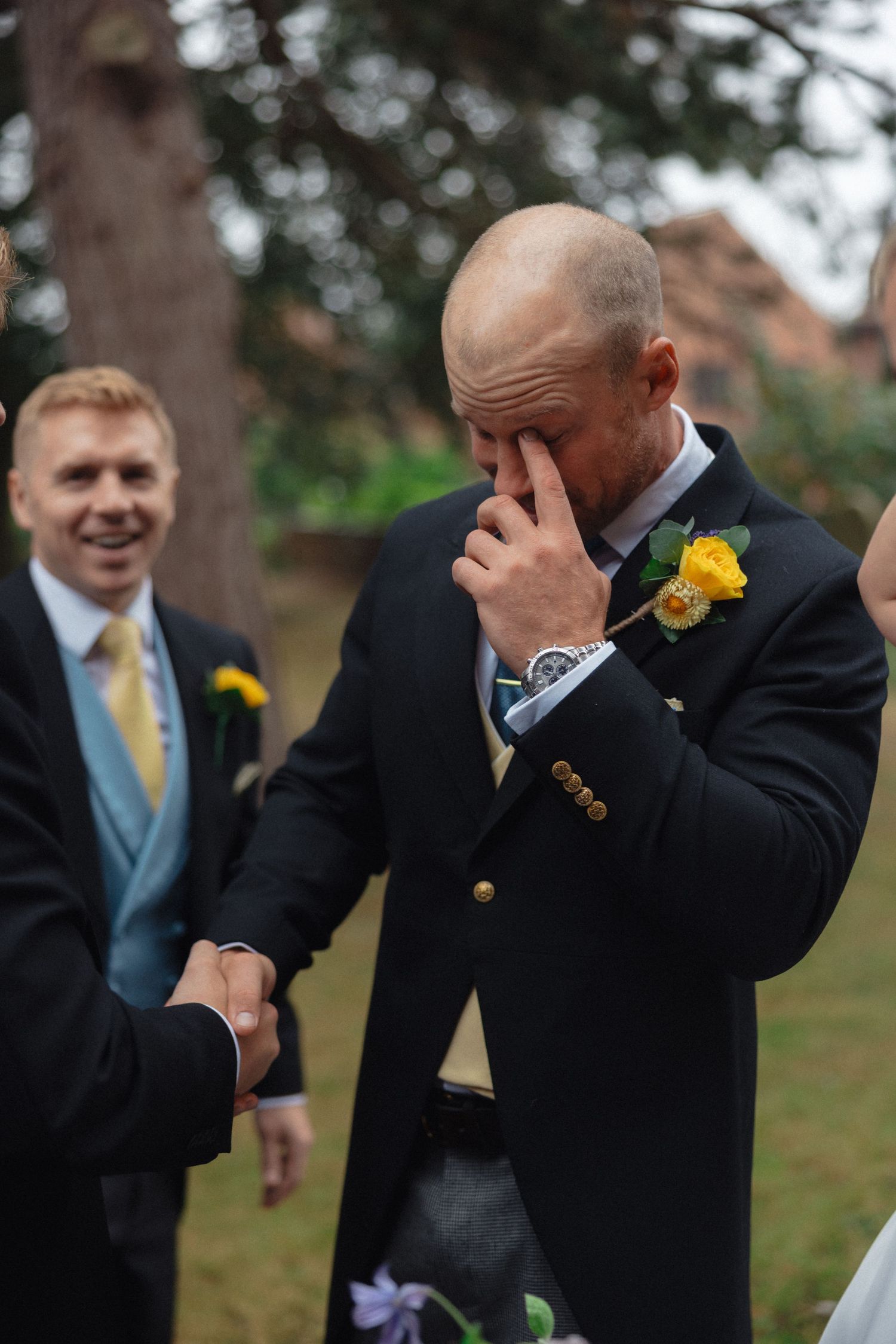 Emotional moment captured during outdoor wedding gathering with yellow boutonniere.