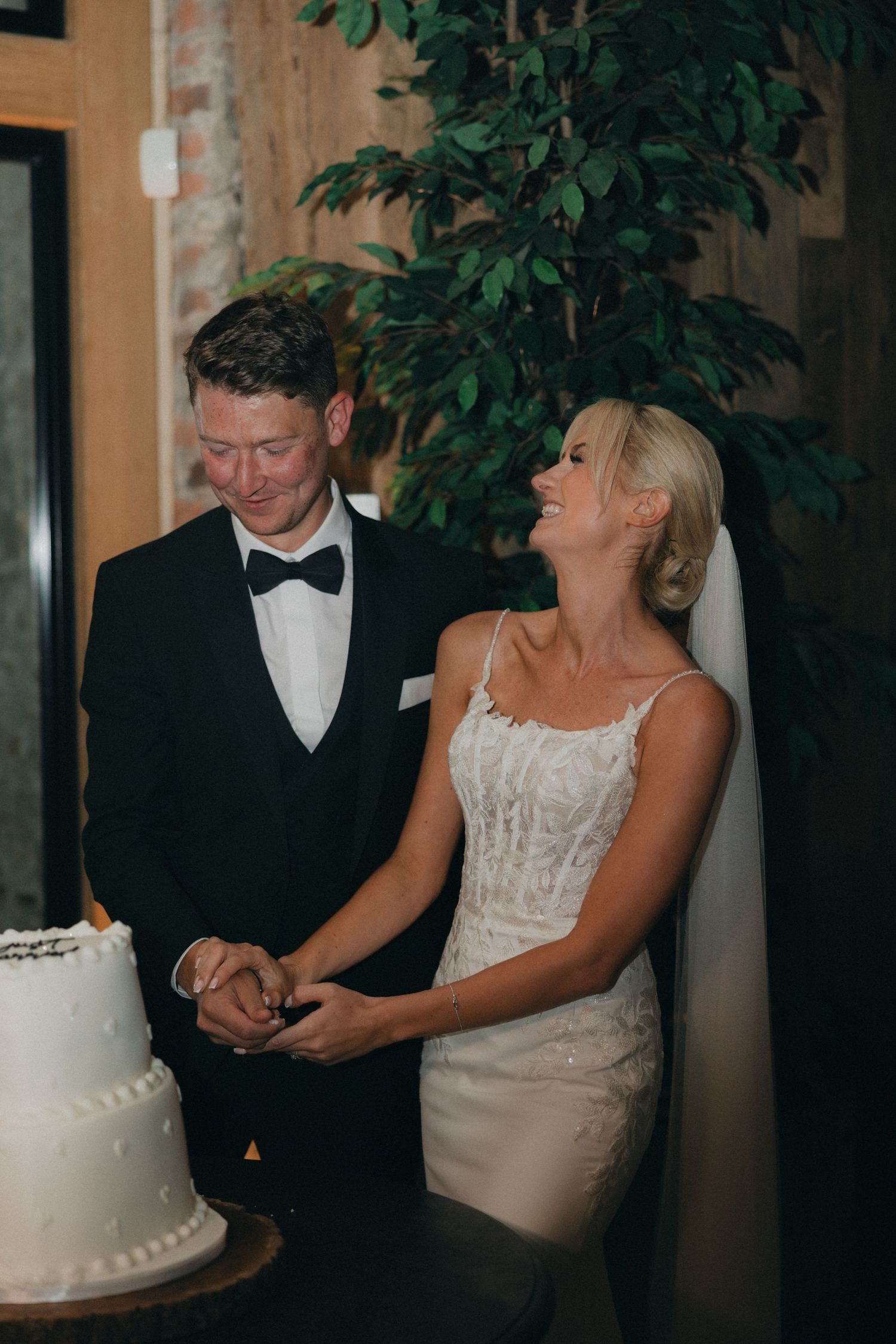 A joyful candid moment between newlyweds standing next to their wedding cake.