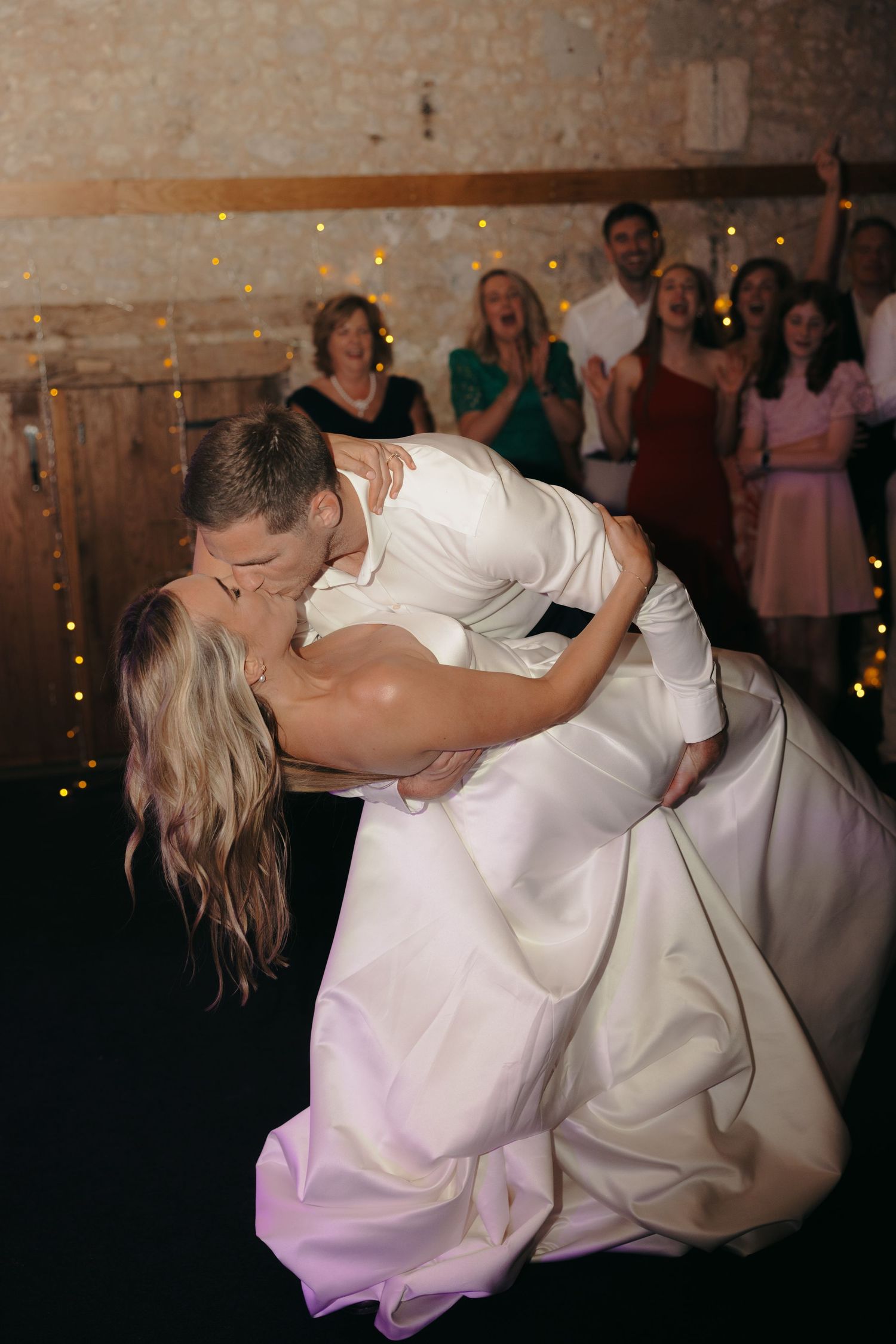 Romantic dip during first dance at wedding reception with stone walls and string lights.