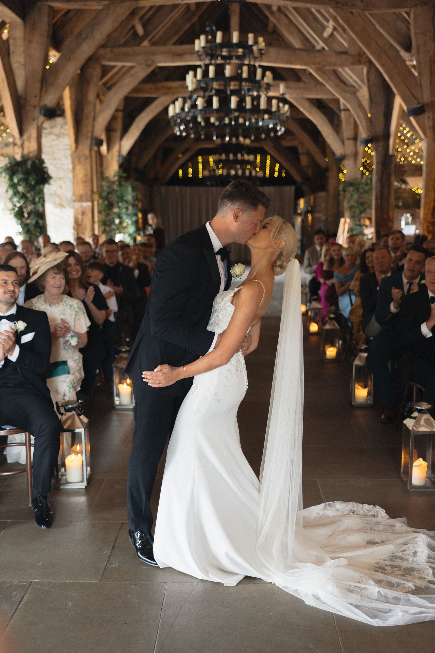Couple sharing their first dance in a beautifully lit rustic barn venue with wooden beams.