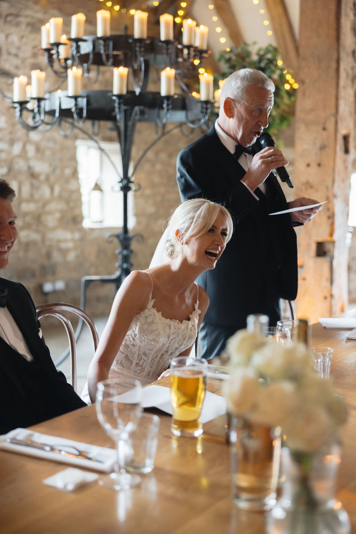 Candlelit wedding reception with guests sharing laughter during speeches.
