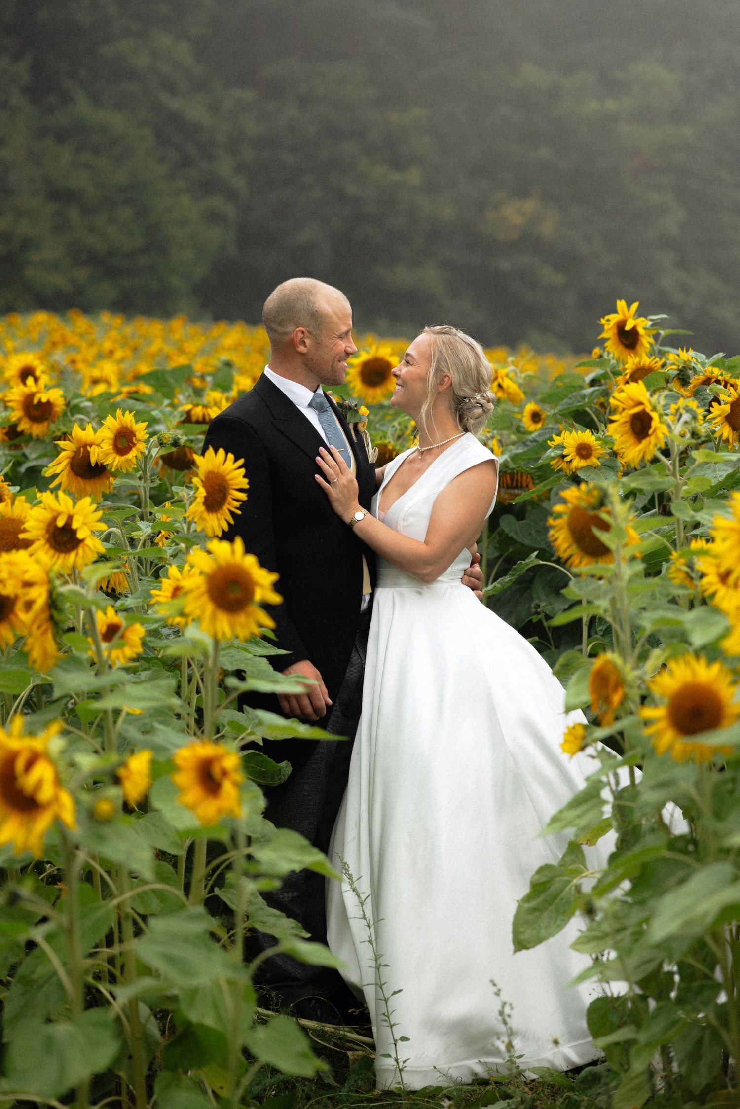 Newlyweds share intimate moment surrounded by towering sunflowers in garden setting.