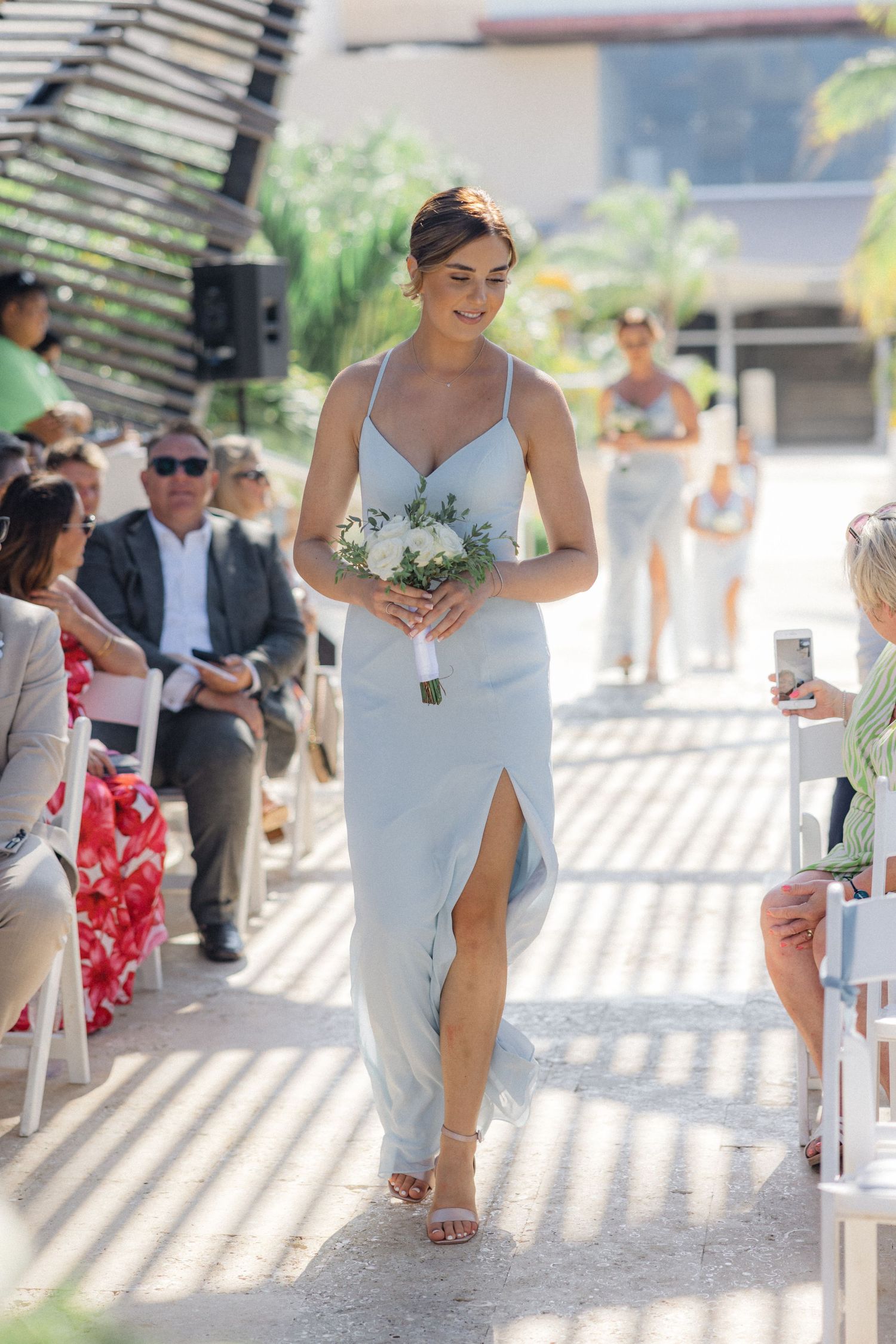 Wedding procession walking down an aisle with striped shadows from overhead pergola.