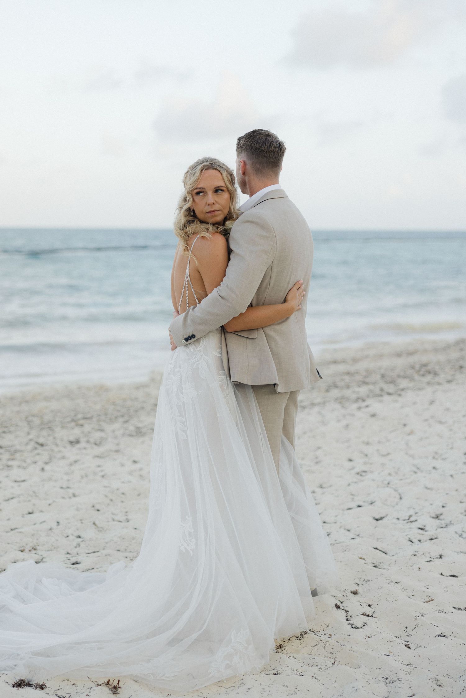 Newlyweds share tender moments on a white sandy beach with flowing wedding dress and ocean views.