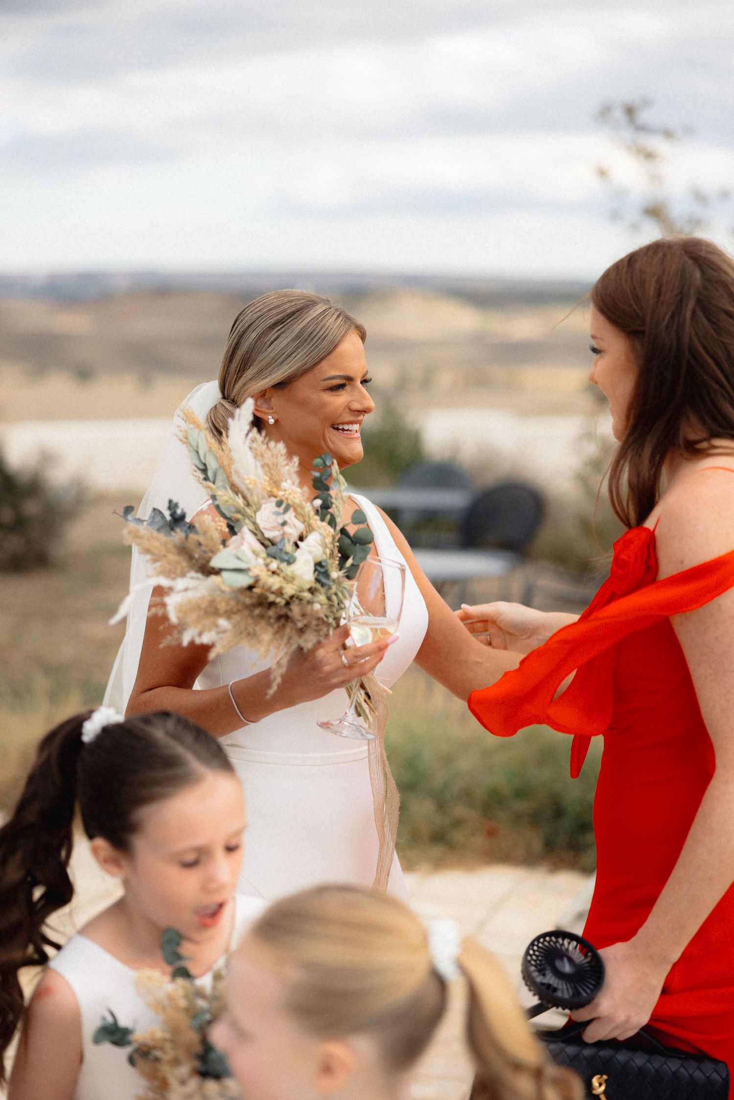 Bride in white dress celebrates with bridesmaids wearing vibrant red dresses outdoors.