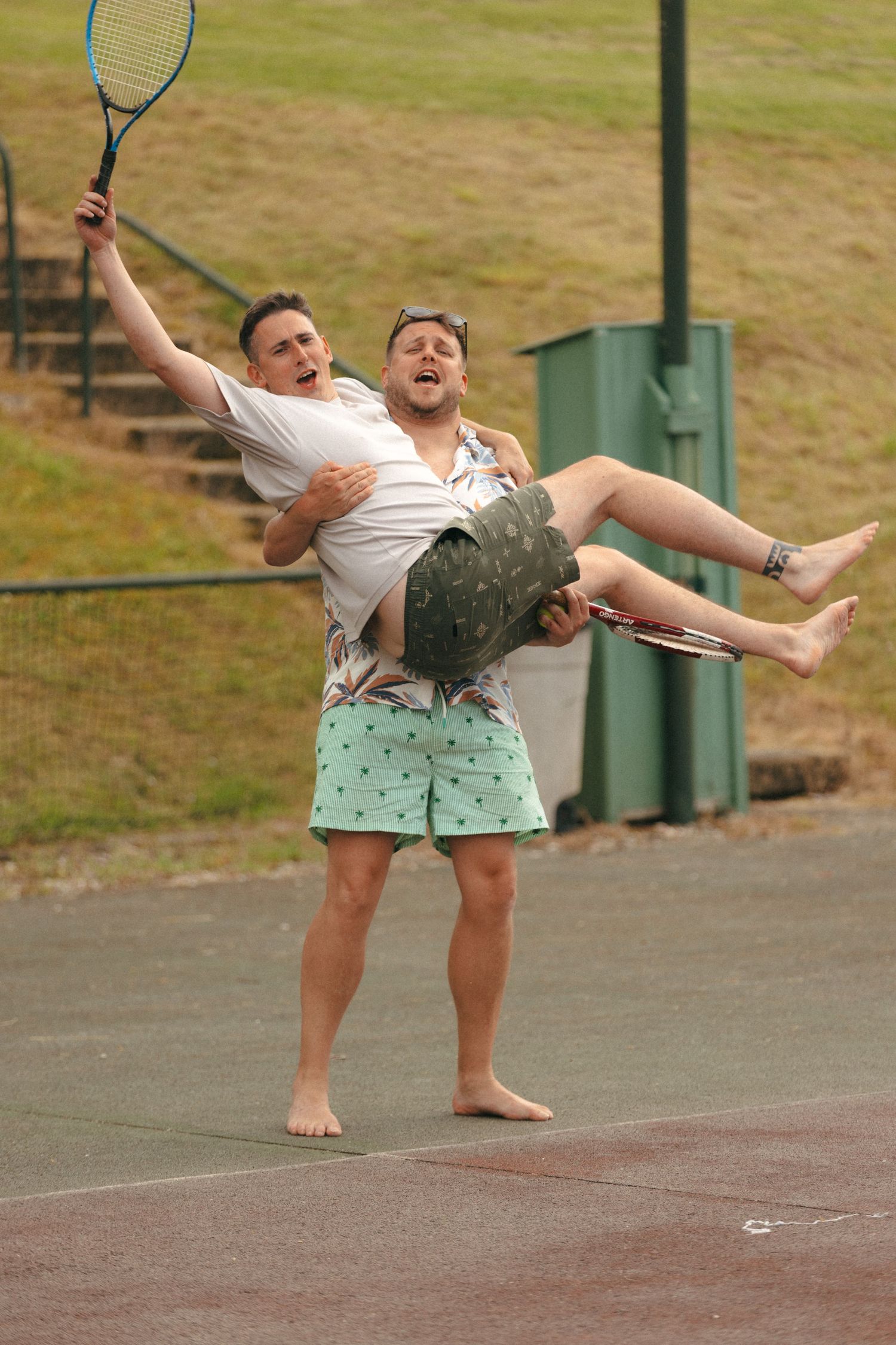 Two people having fun on a tennis court with one carrying the other in a playful pose.