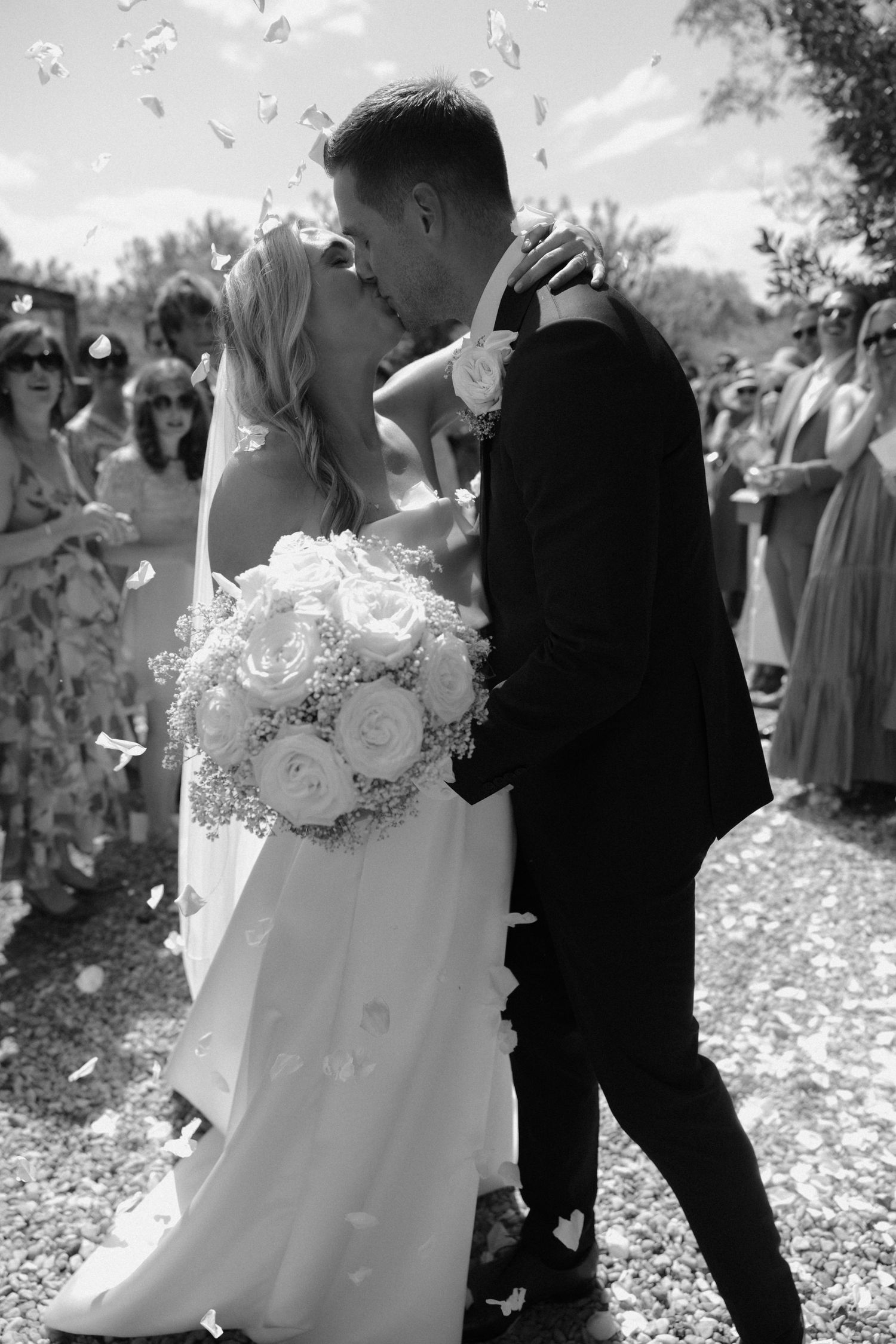 Black and white photo of couple walking through flower petals at outdoor wedding.