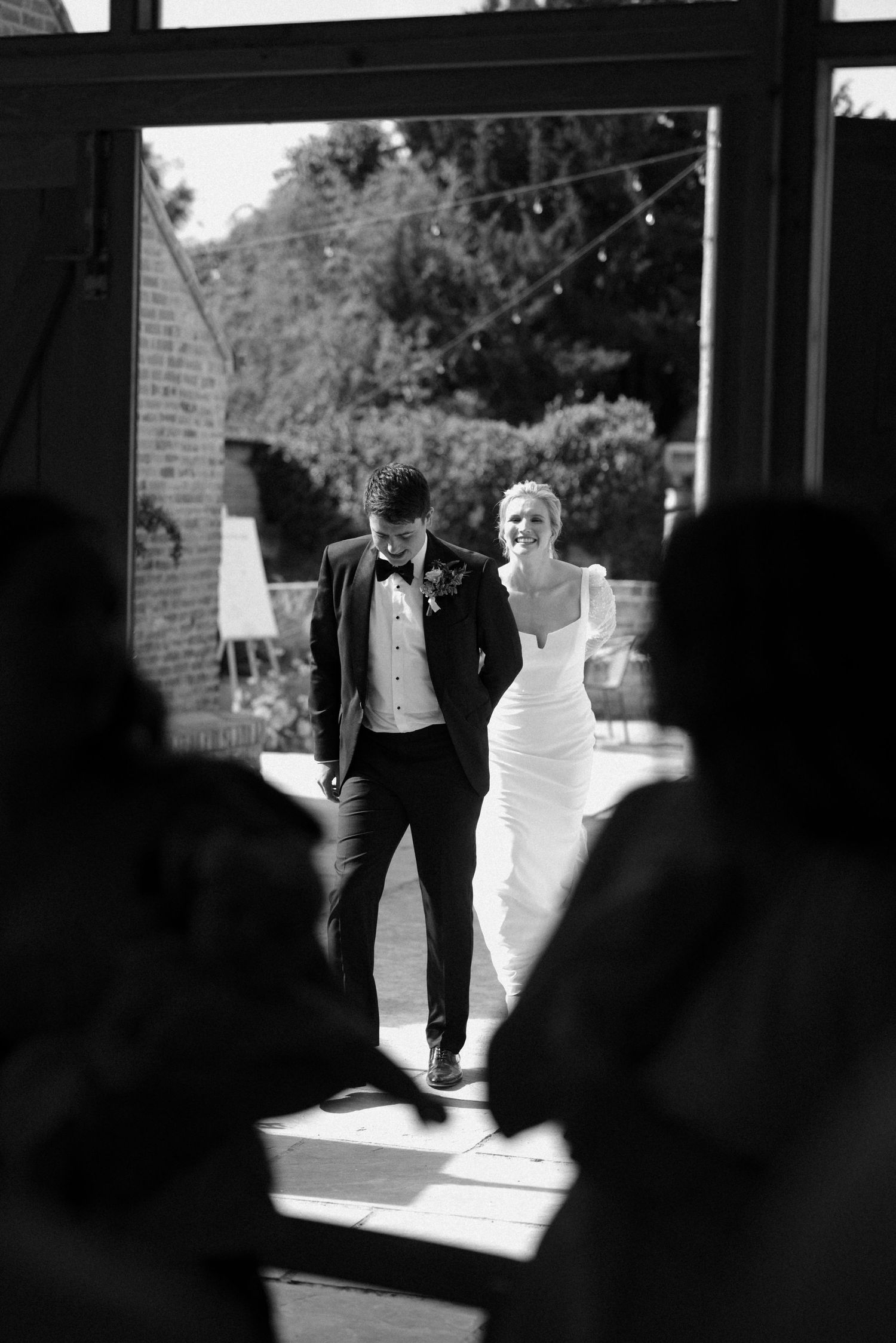 Dramatic black and white silhouette of wedding party entering through doorway.