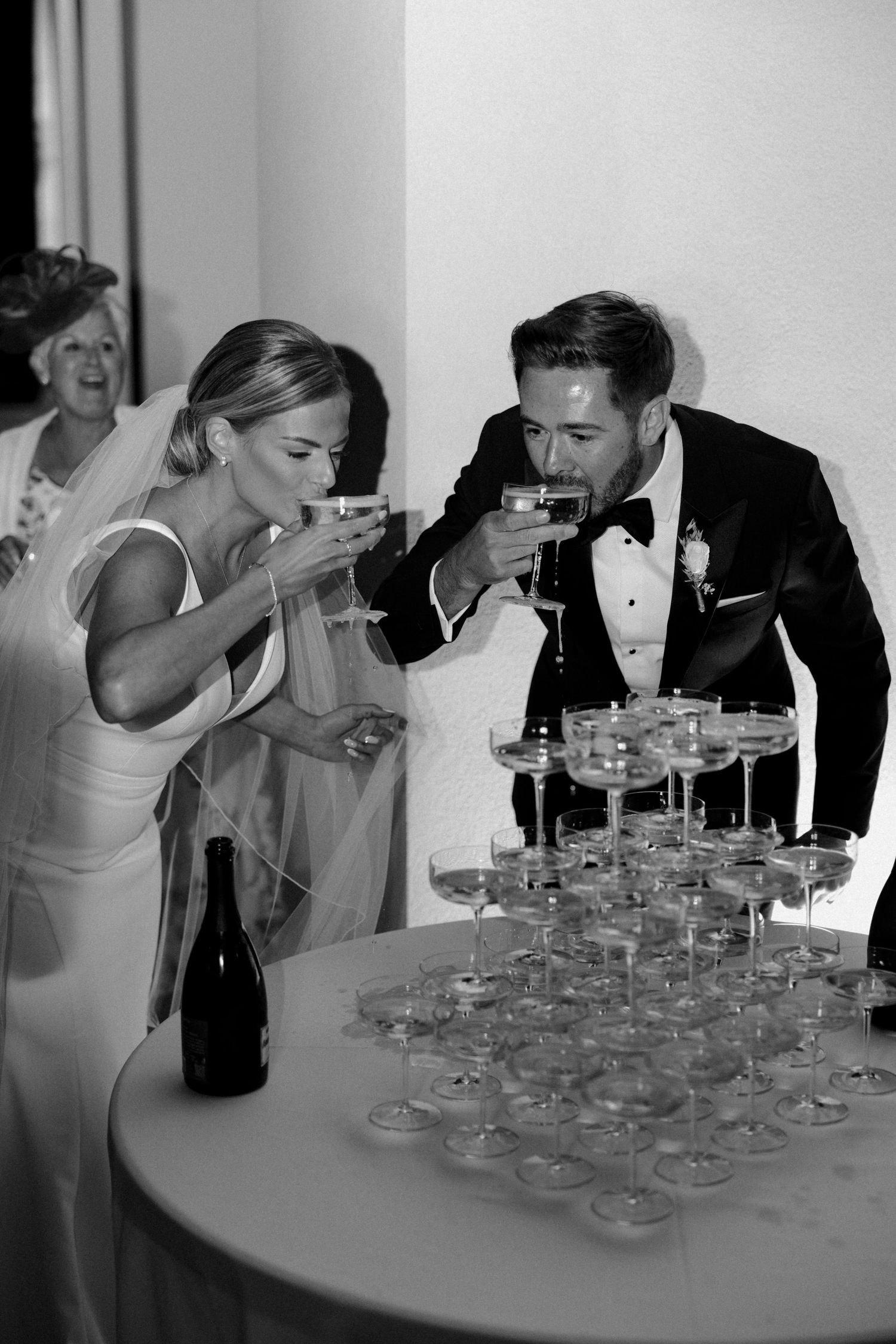 Candid moments of a couple attempting to pour champagne into stacked glasses.