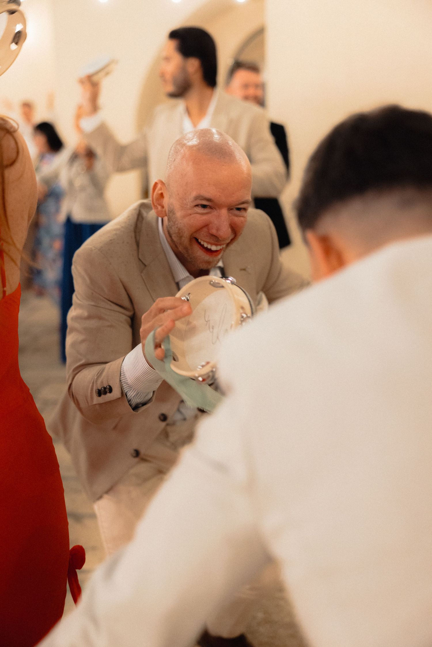 Wedding guests laugh and celebrate during a reception in a warmly lit indoor venue.