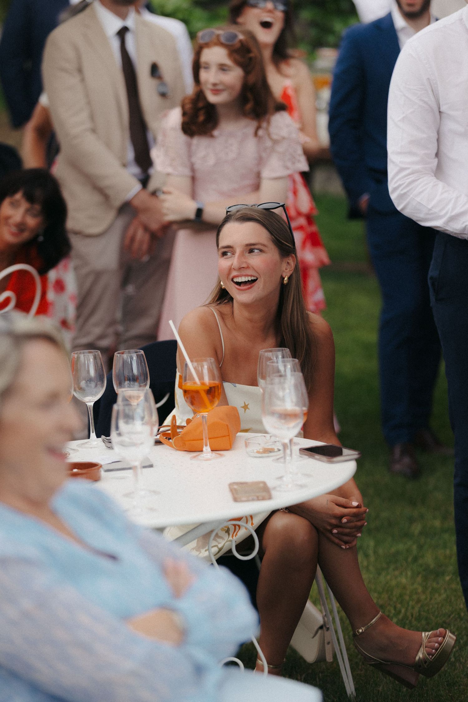 Outdoor wedding reception with guests seated at tables with wine glasses and orange decor.