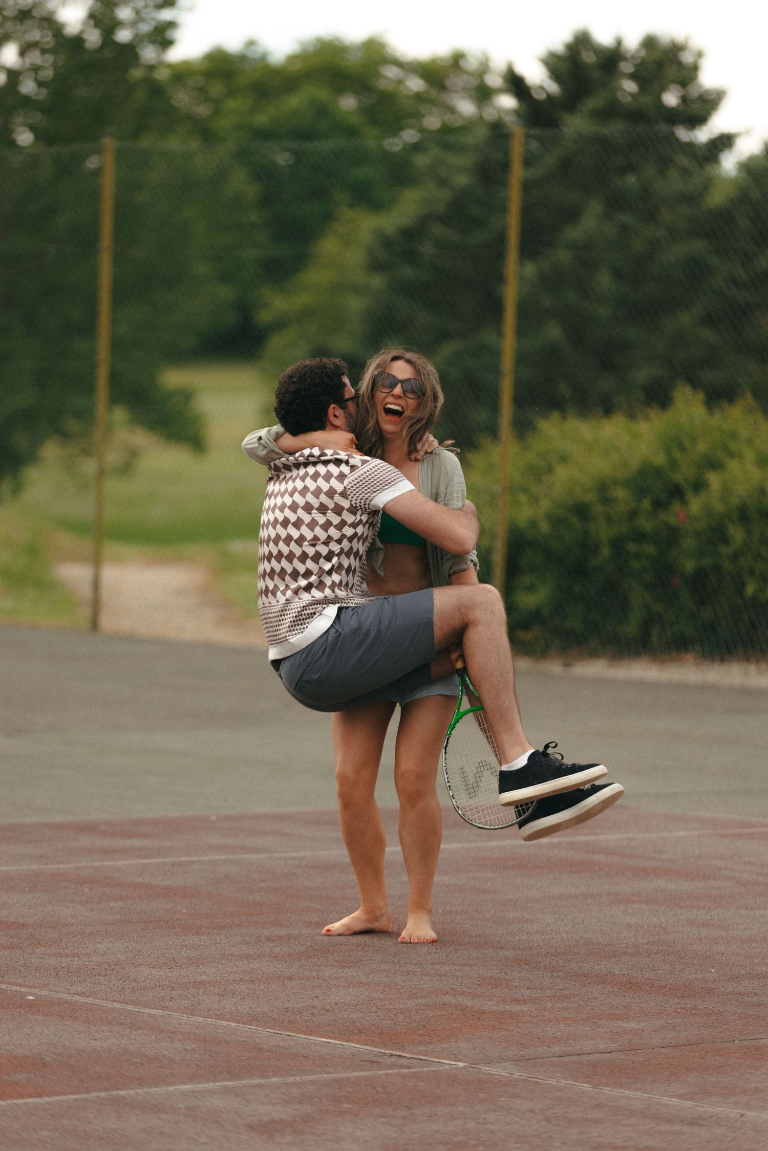 Two people sharing a playful moment while spinning on a tennis court.