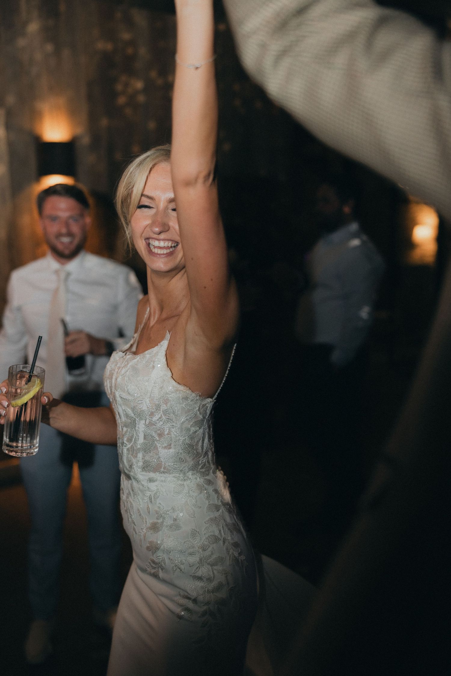 A bride in white dress joyfully dancing with raised arms at her wedding reception.