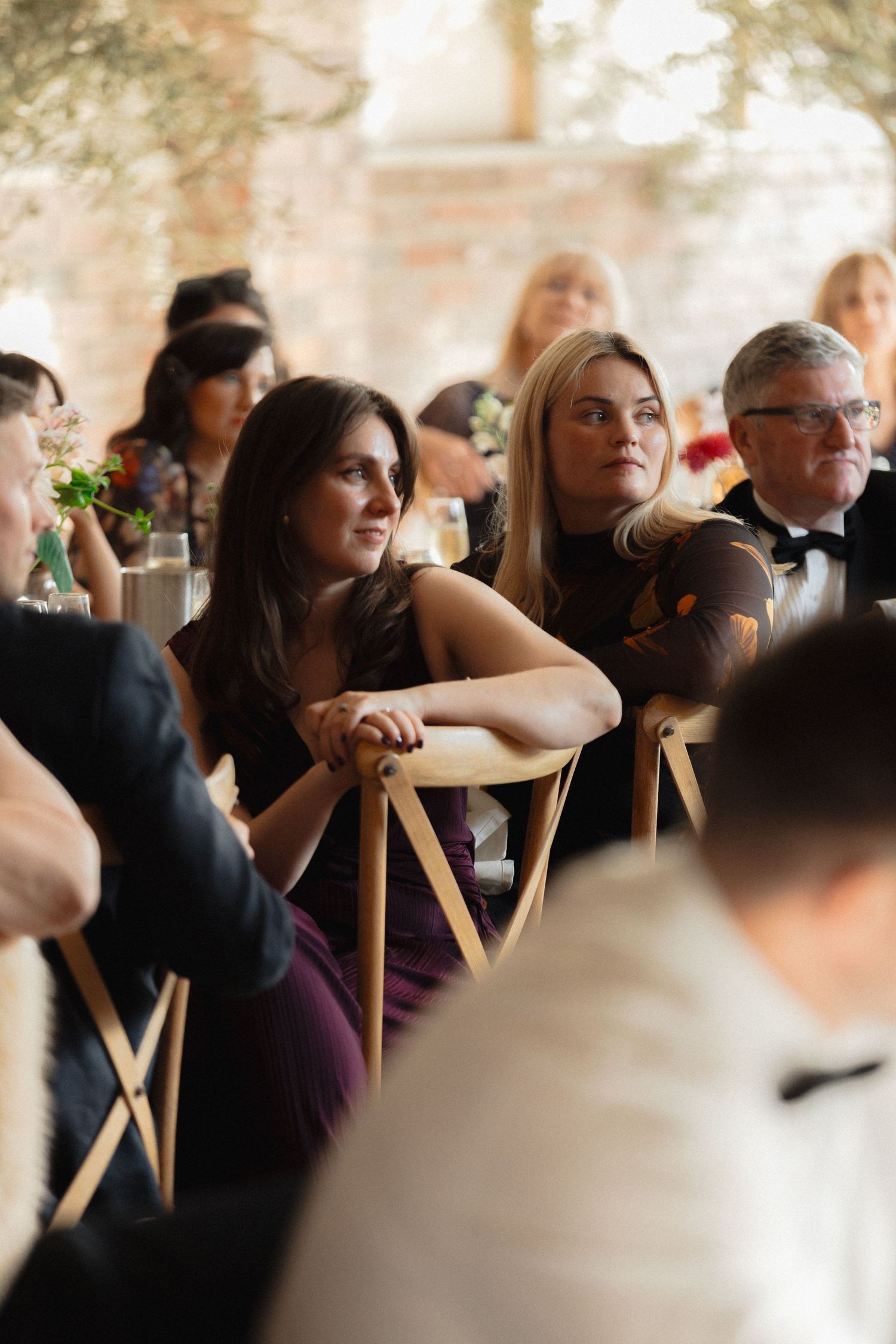 Wedding guests seated at tables during a reception in a rustic venue with exposed brick walls.