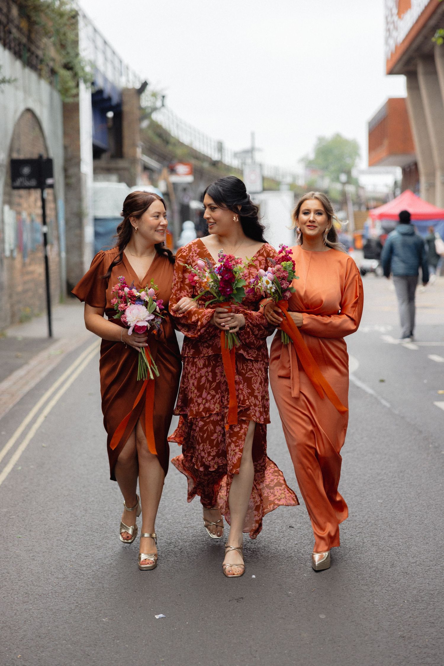 Wedding party in vibrant rust-colored dresses walking down an urban street.