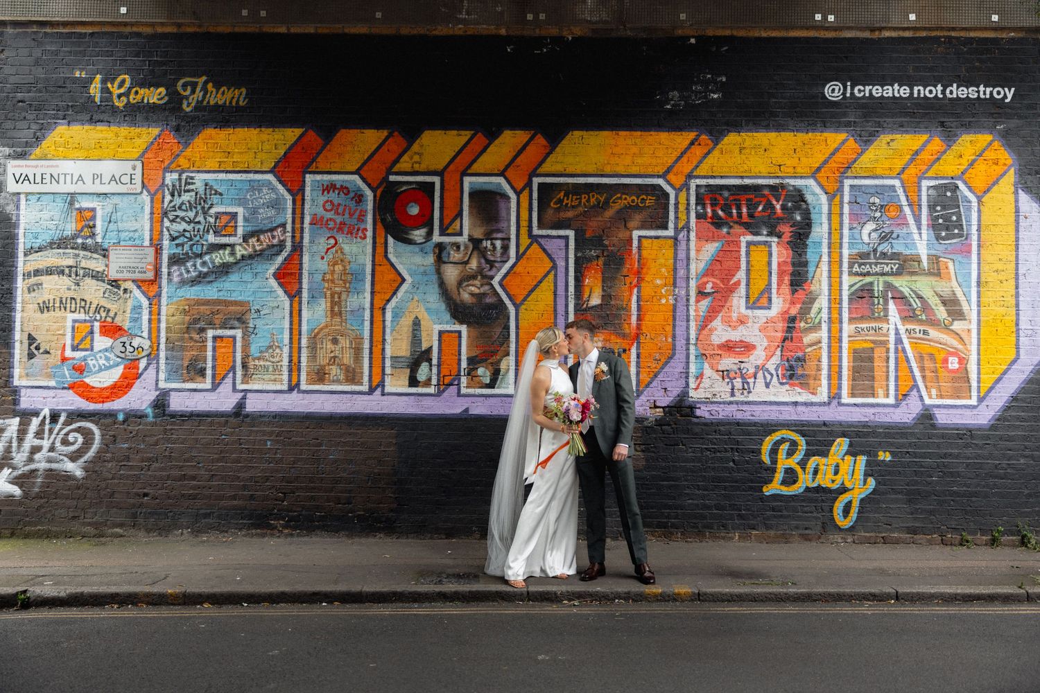 A wedding couple poses against a colorful graffiti wall creating an urban artistic backdrop.
