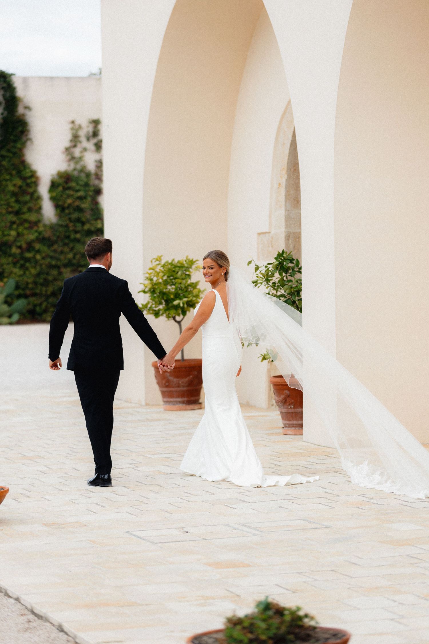 Romantic wedding photos in a sun-lit colonnade with cream colored arches.