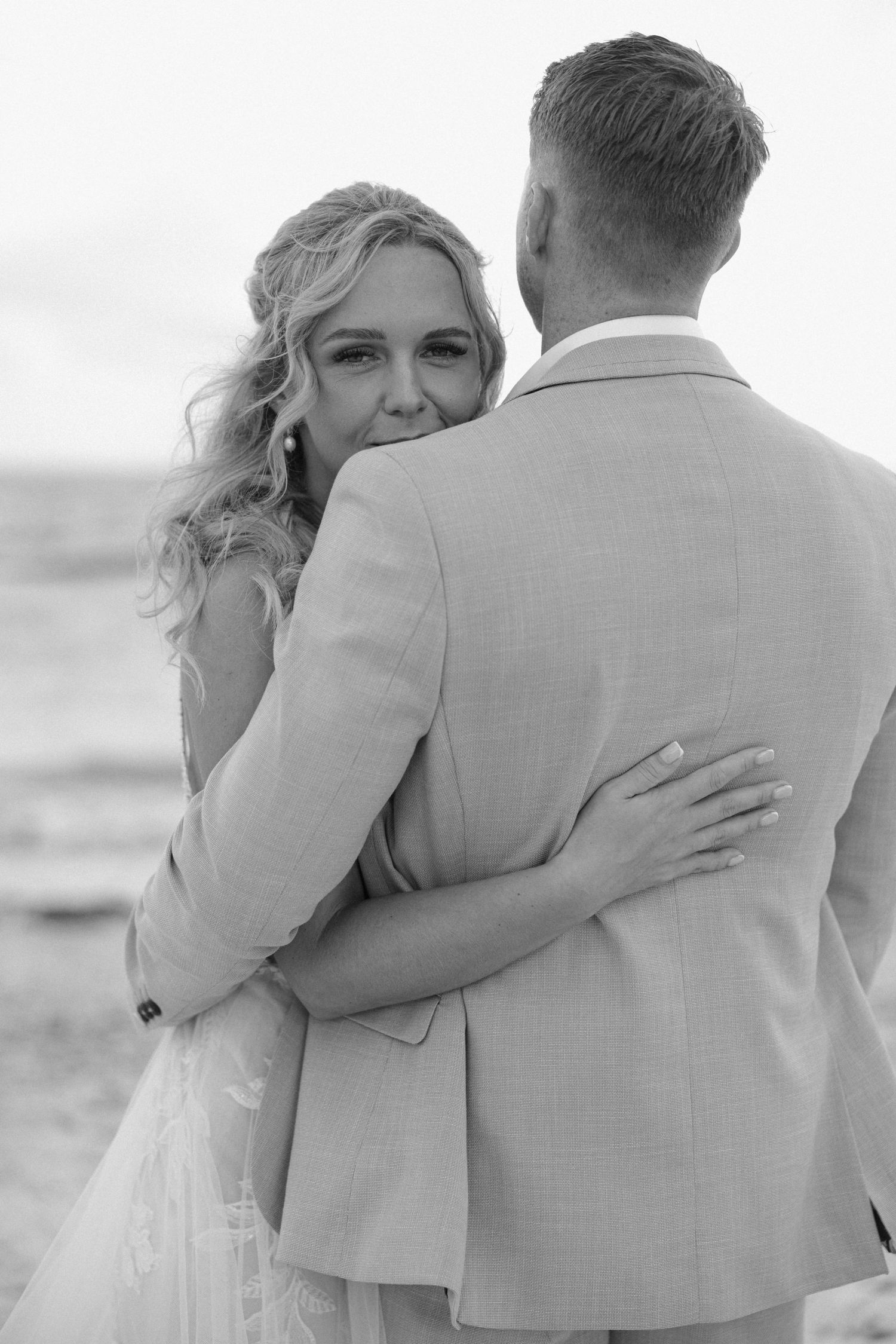 Black and white series of romantic beach wedding photos capturing close embraces.
