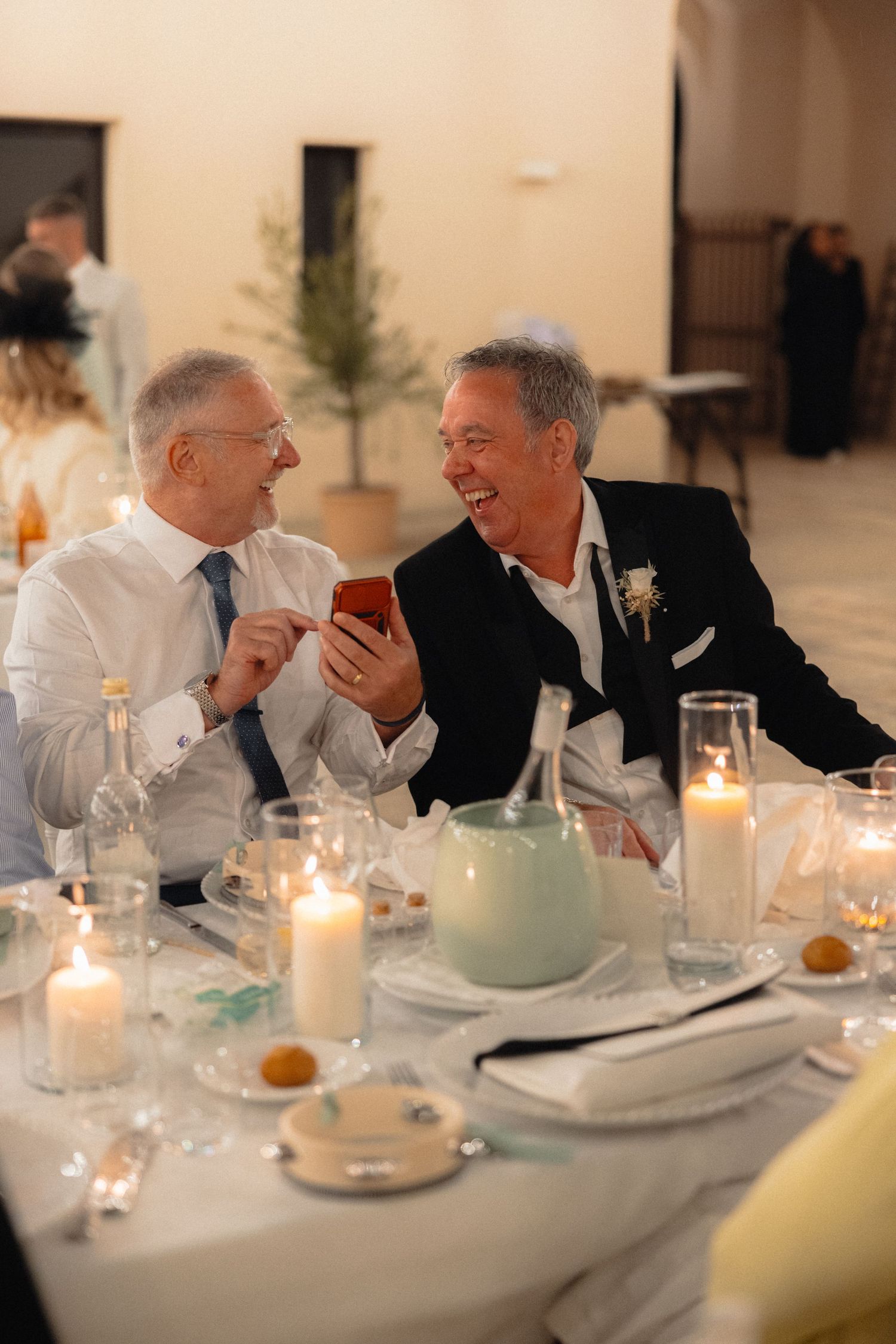 Candlelit wedding reception table with guests engaged in lively conversation.