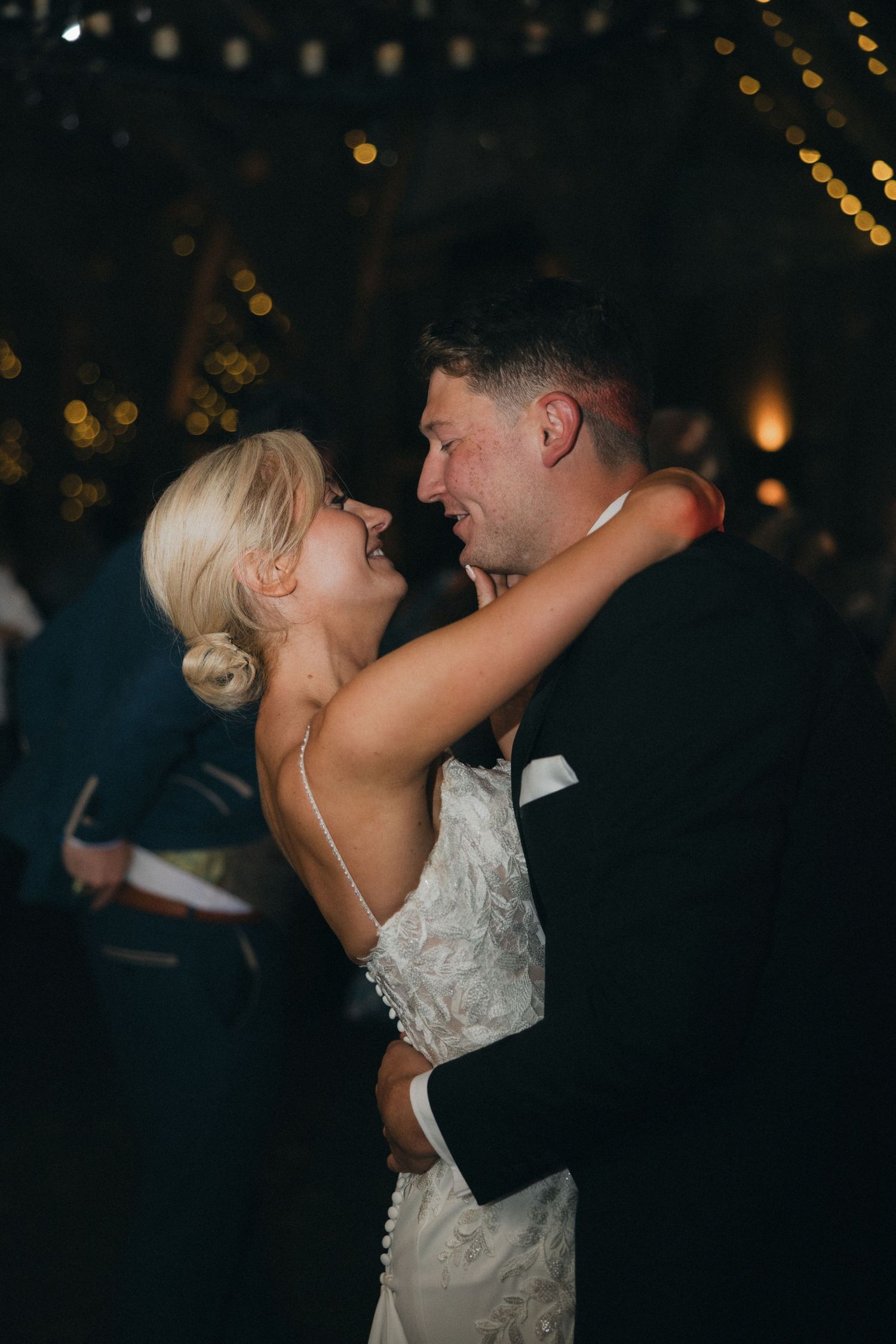 A couple shares a romantic dance moment at their wedding reception with twinkling lights in background.