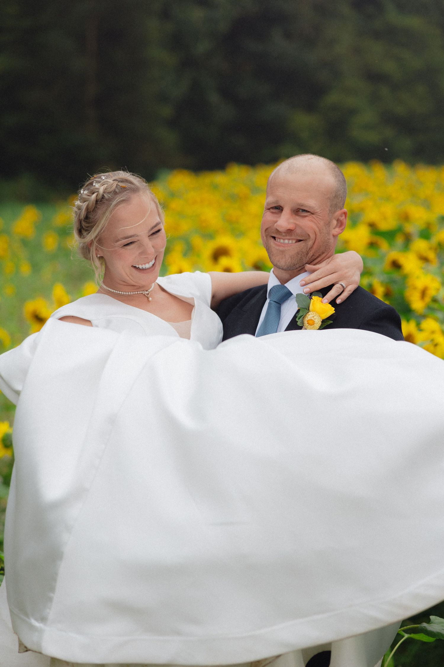 Romantic wedding couple embraces in front of vibrant sunflower field with flowing white veil.