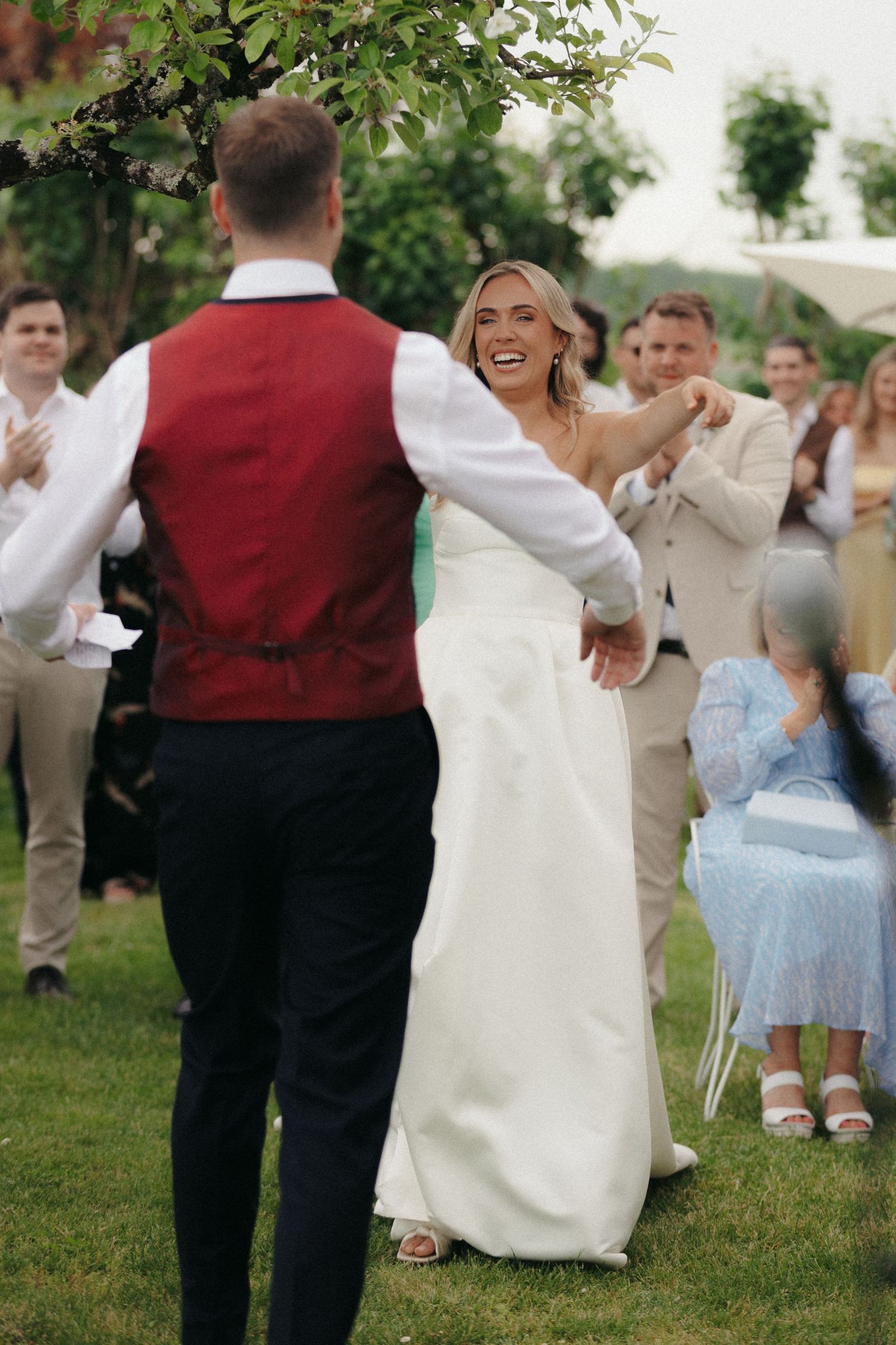 Wedding party members celebrate on a grassy lawn with formal attire and white dresses.