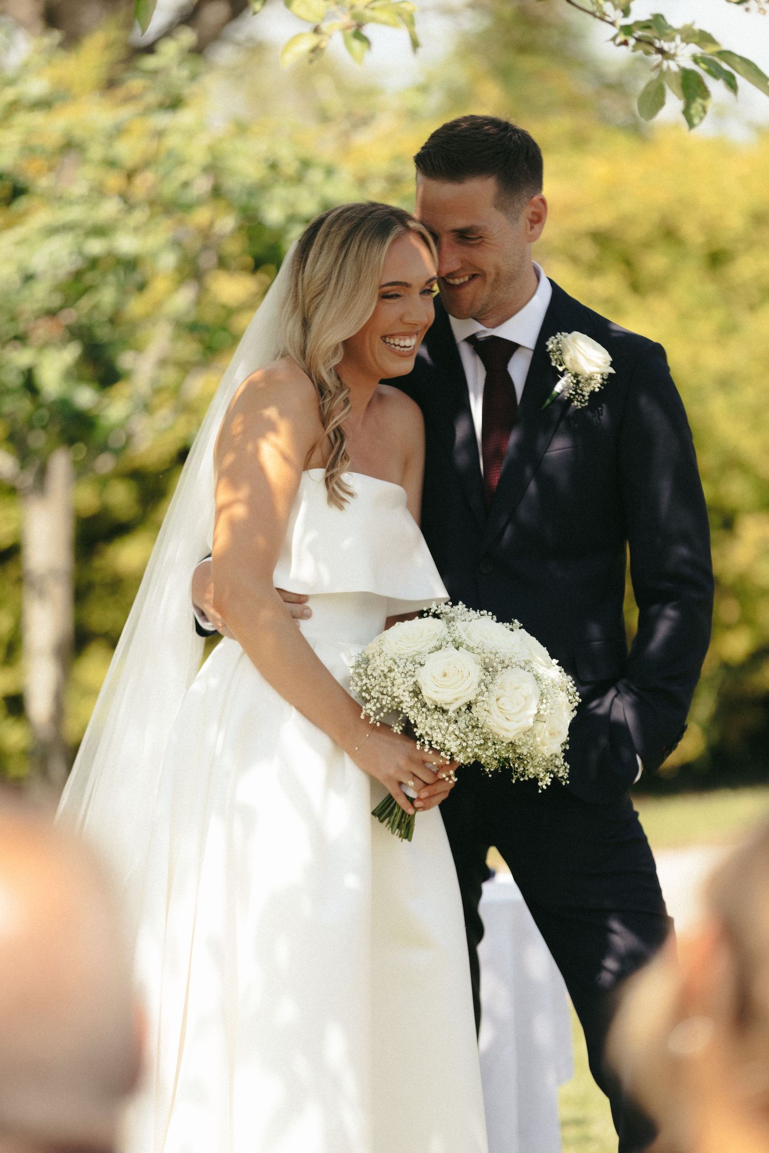 A romantic wedding moment with a couple embracing while holding a white floral bouquet.