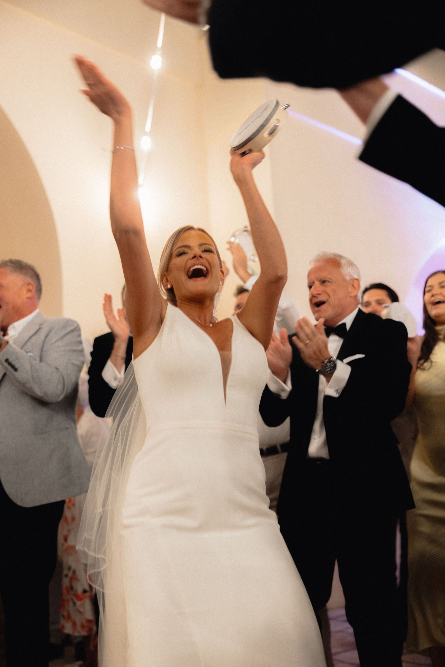 Wedding celebration with guests raising their arms in excitement on a dance floor.