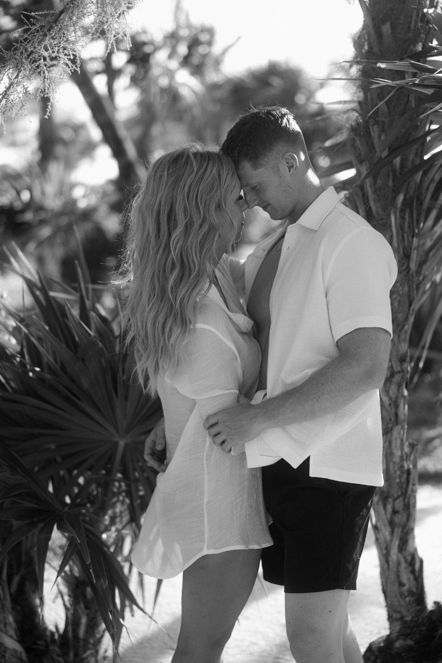 A black and white romantic portrait of a couple among tropical palm fronds.