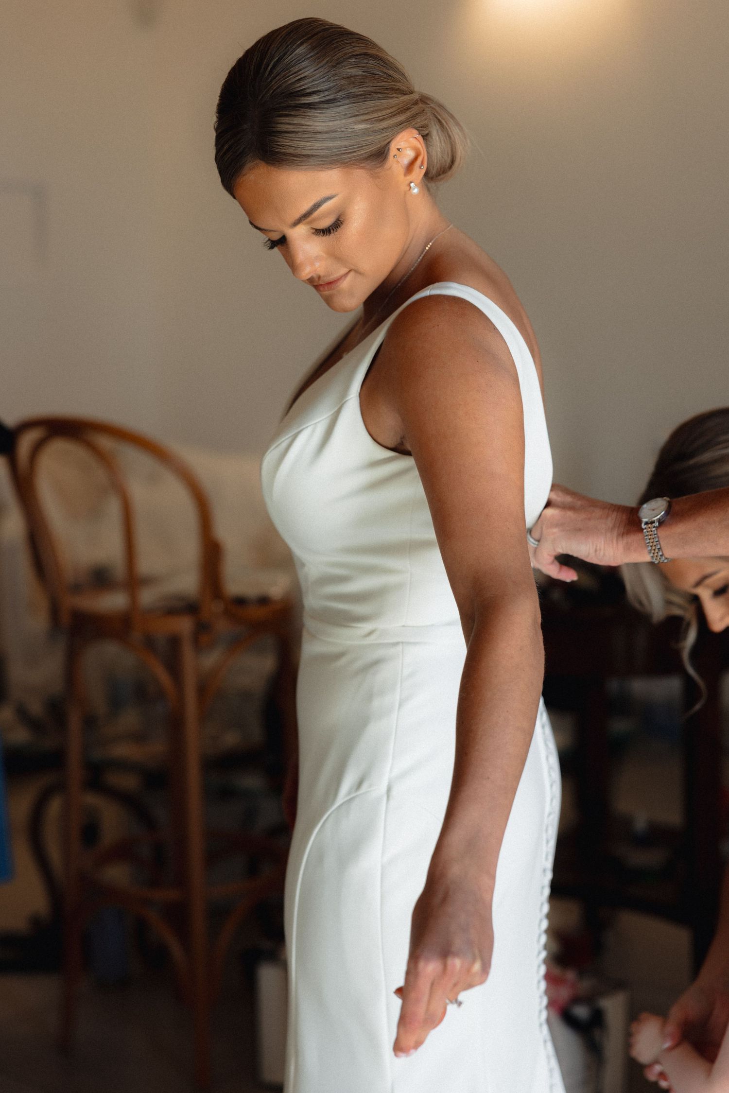 Elegant white wedding dress being fitted in natural window light.