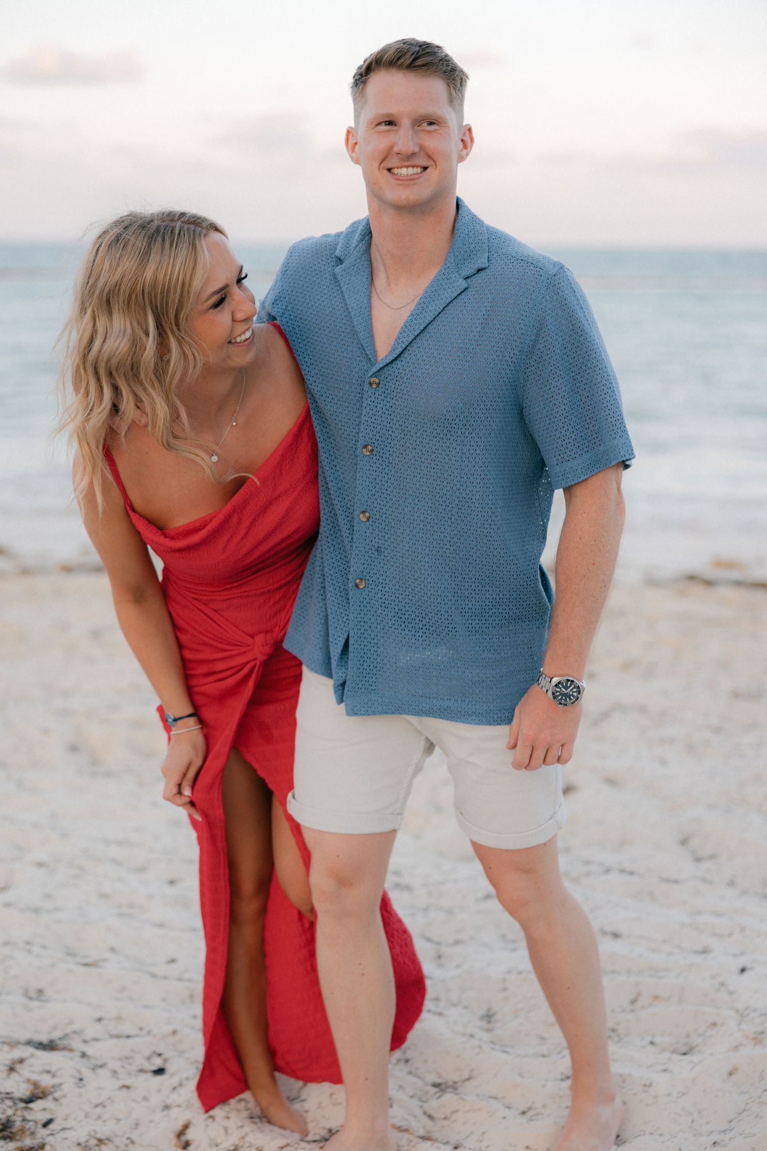 A couple in blue and red outfits playfully posing together on a sunny beach.