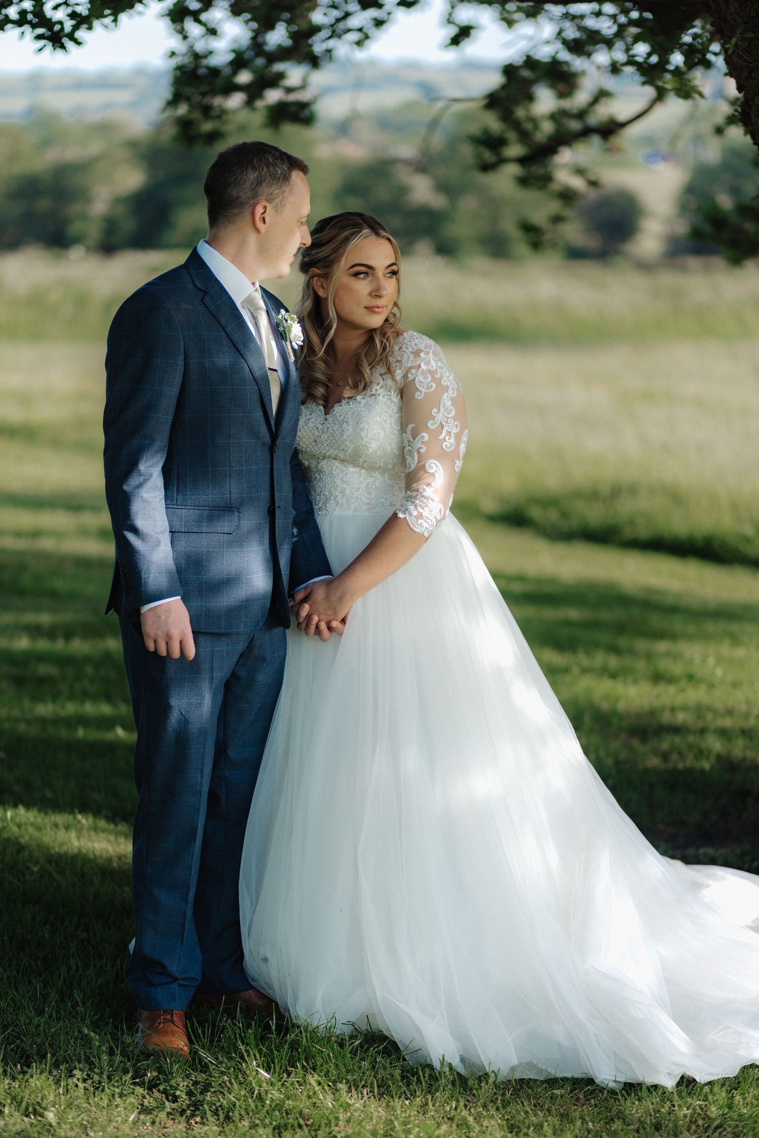 Romantic wedding photos captured in a sunlit meadow with rolling hills in the distance.