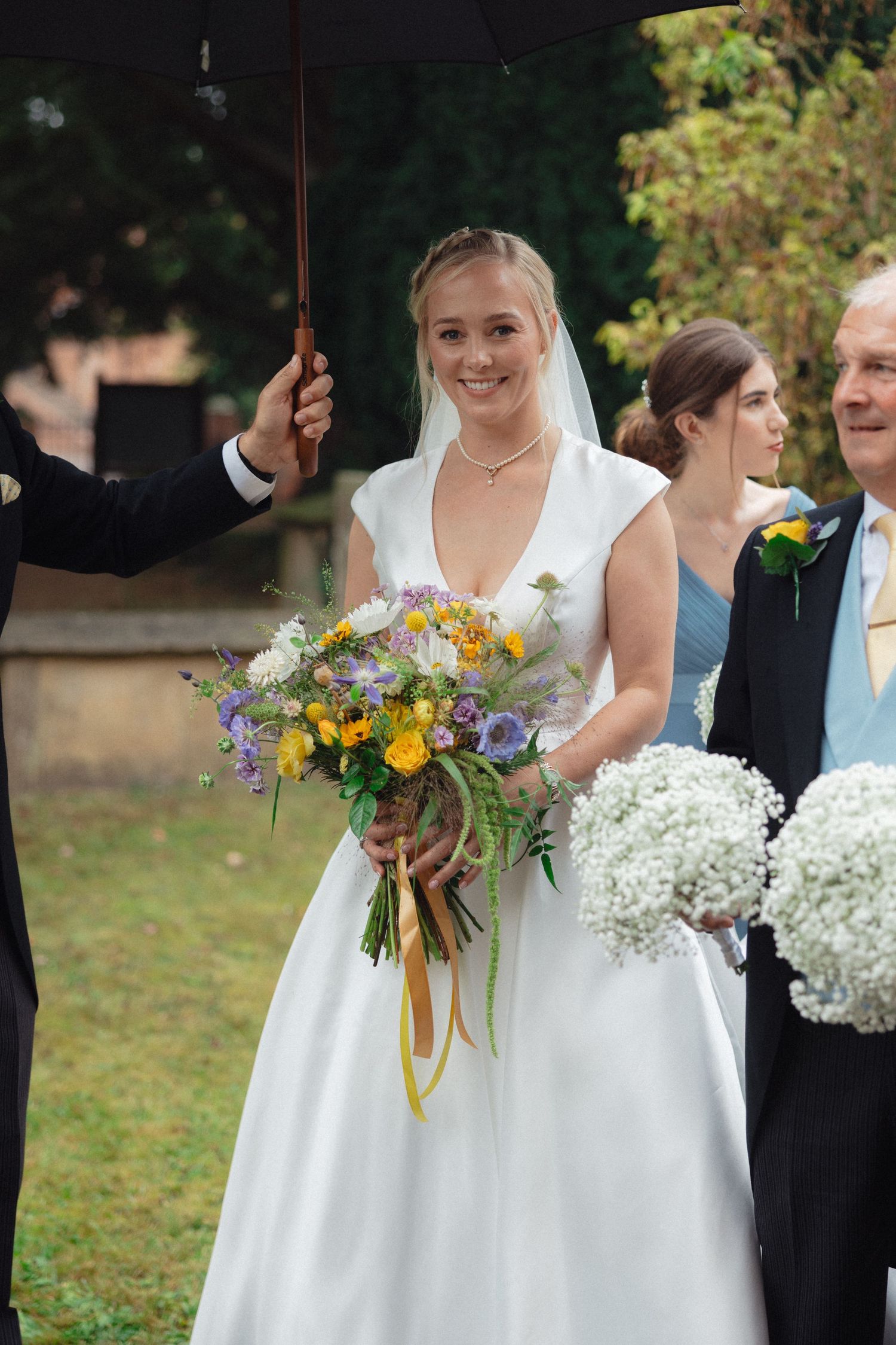 Wedding party holding beautiful bouquets of white hydrangeas and yellow flowers against an outdoor backdrop.