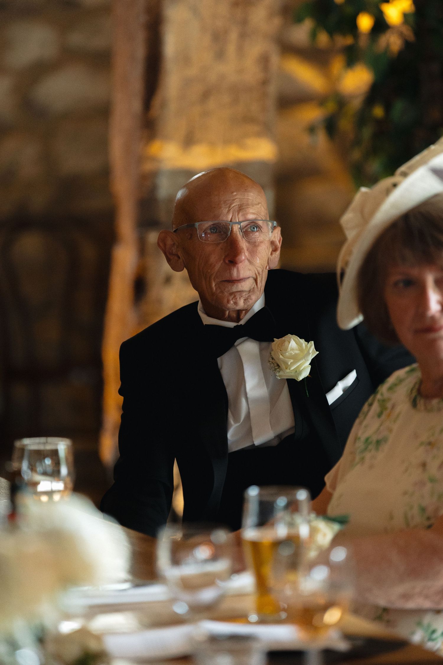 Guests seated at a formal dining table with stone walls and warm lighting in the background.