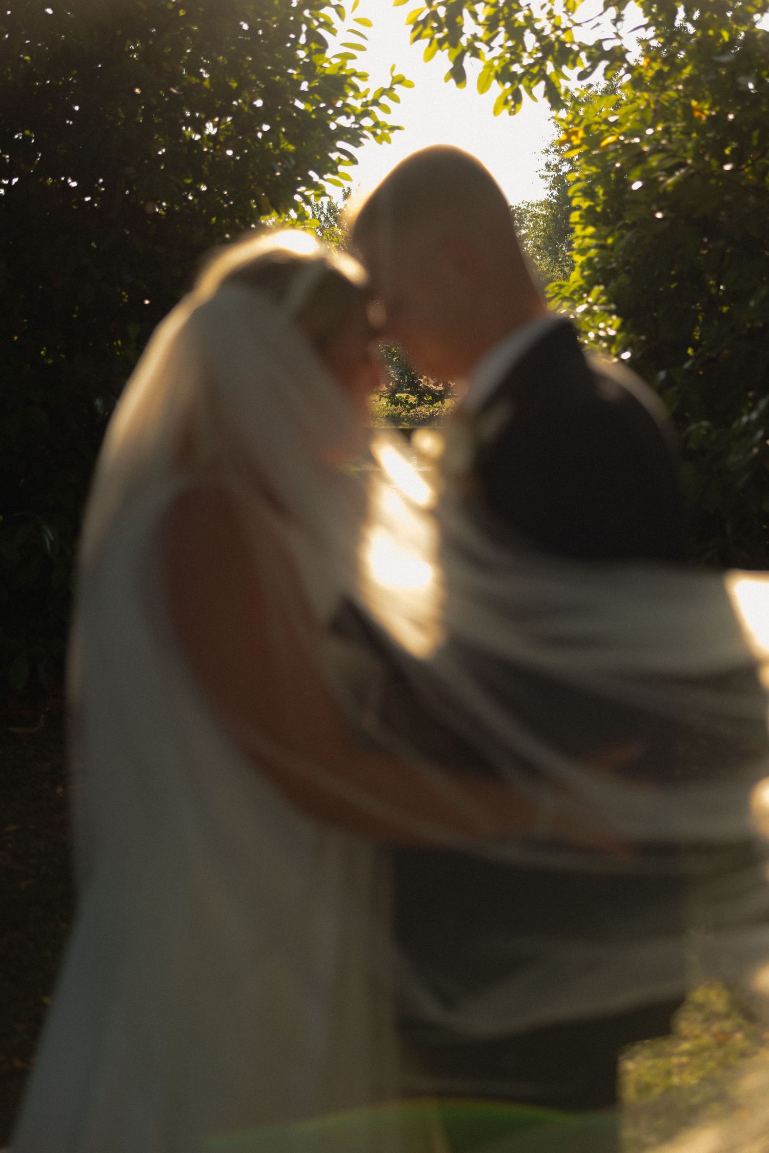 Romantic sunset wedding portrait with sunlight filtering through trees.