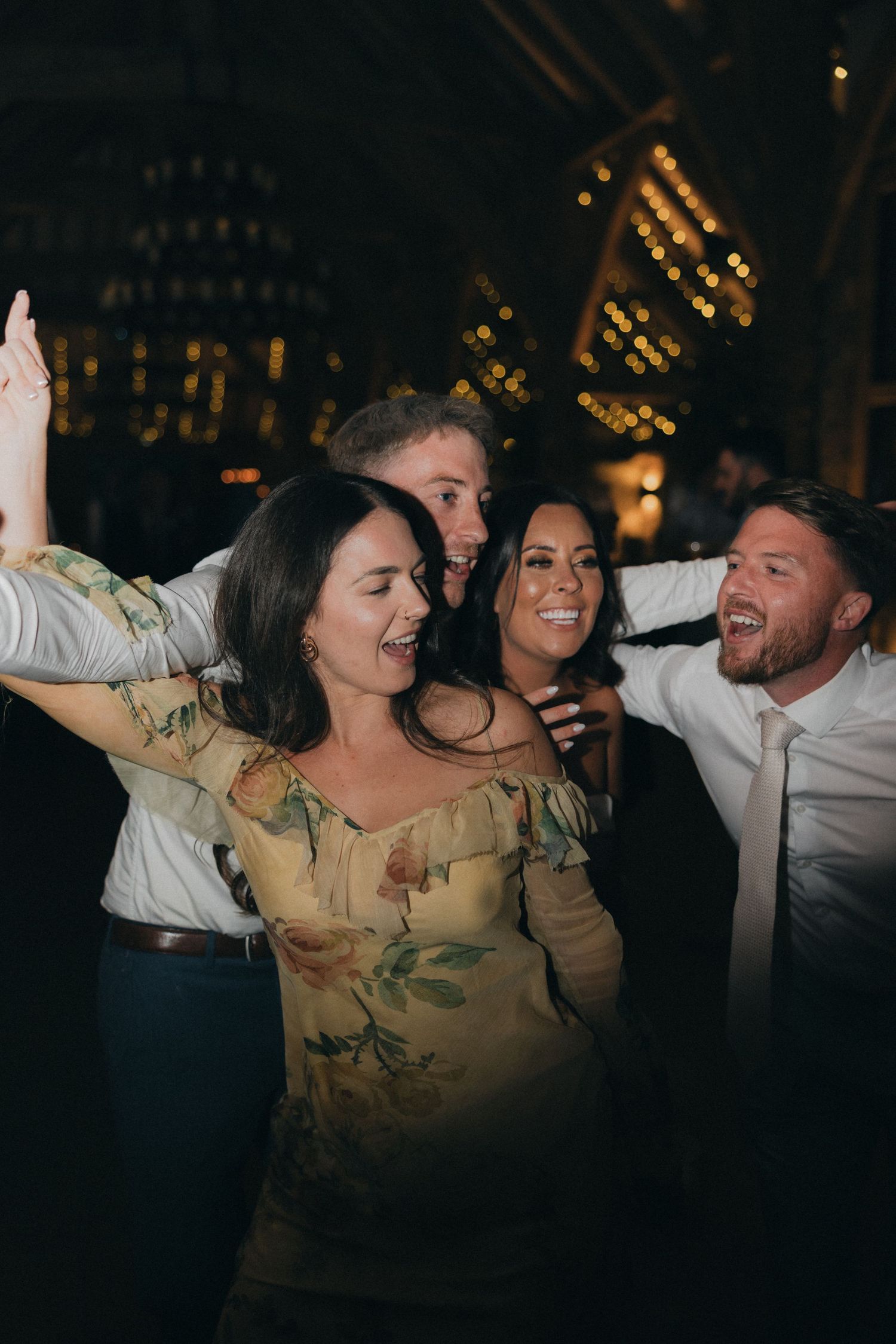Wedding guests dance and celebrate with arms raised at a lively reception.
