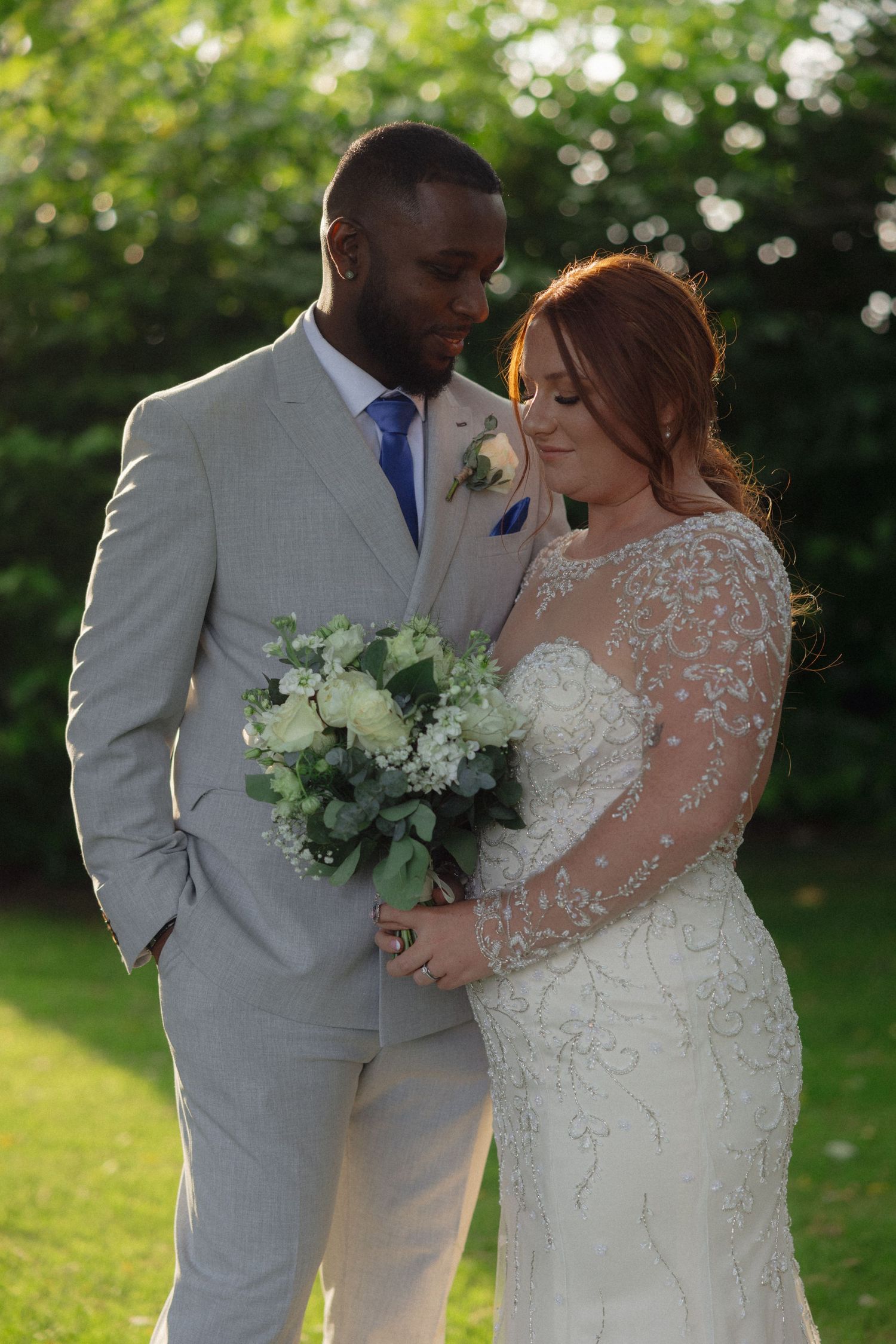 Newlyweds in elegant white attire sharing an intimate moment in a sunlit garden.