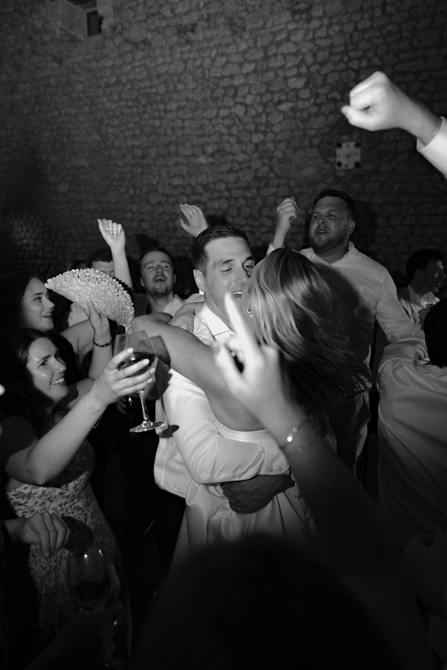 Wedding guests dancing and celebrating in a rustic brick-walled venue.