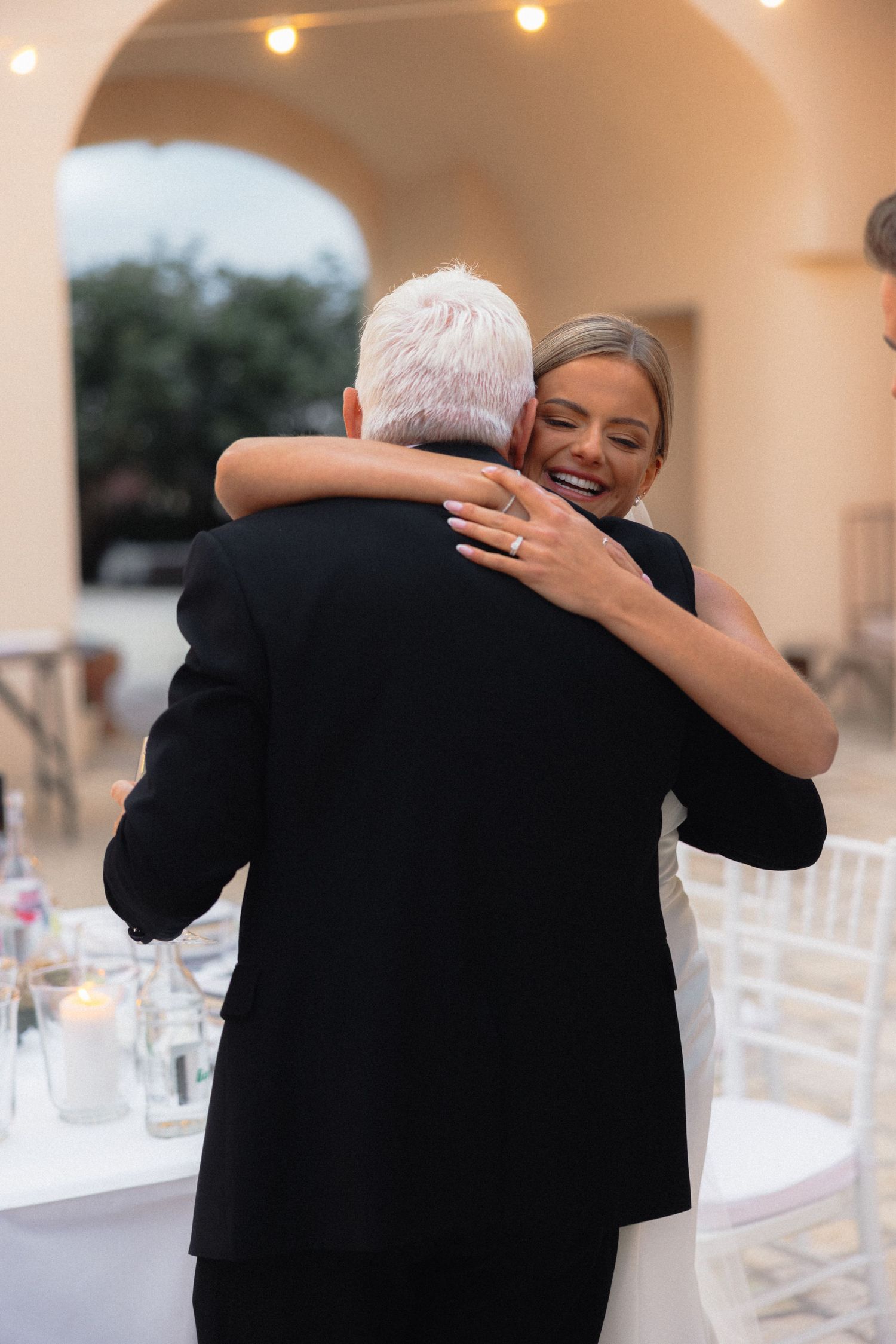 Emotional embrace during wedding reception with white tables and chairs in background.