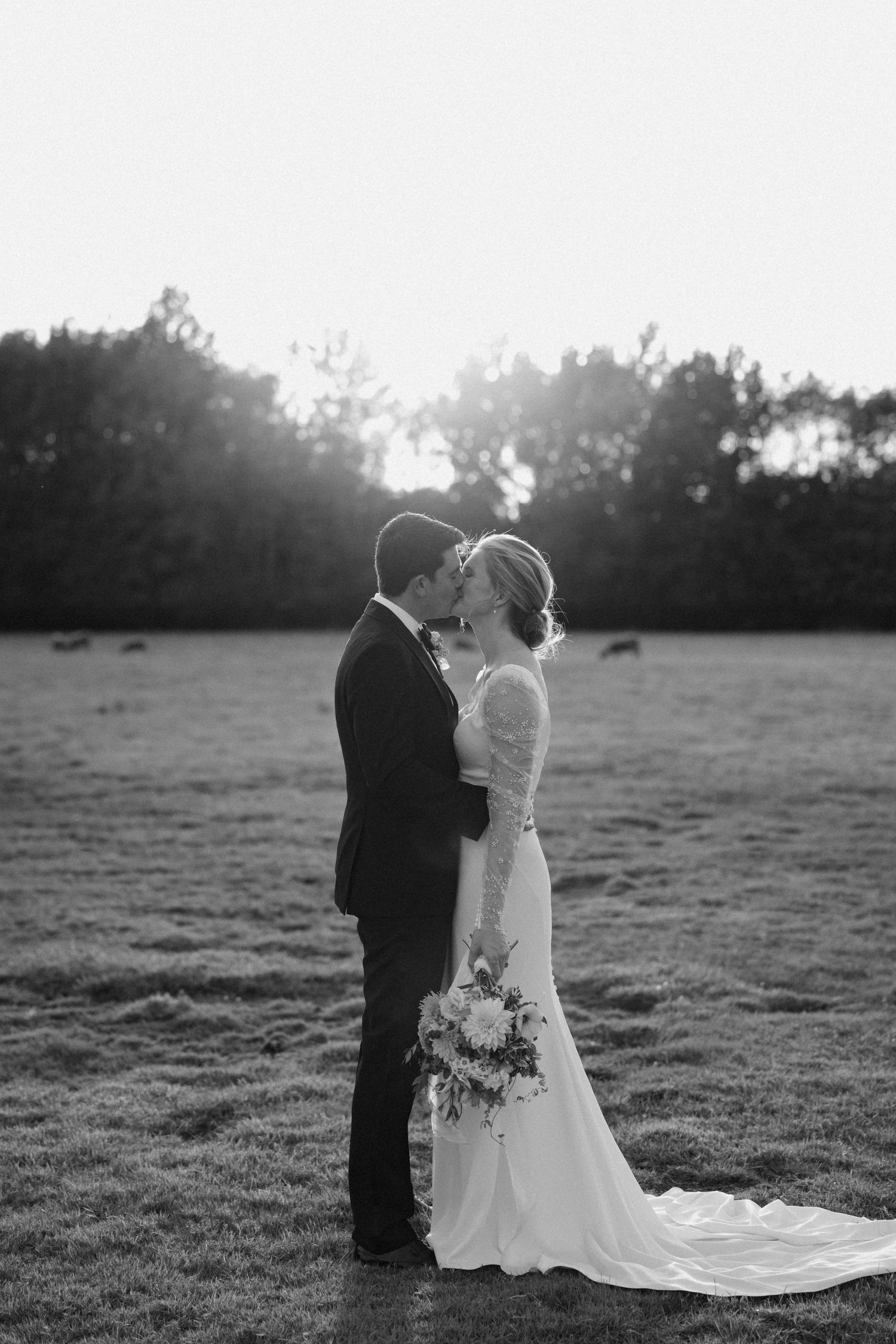 Black and white portrait of newlyweds in a sunlit meadow with flowing wedding dress.