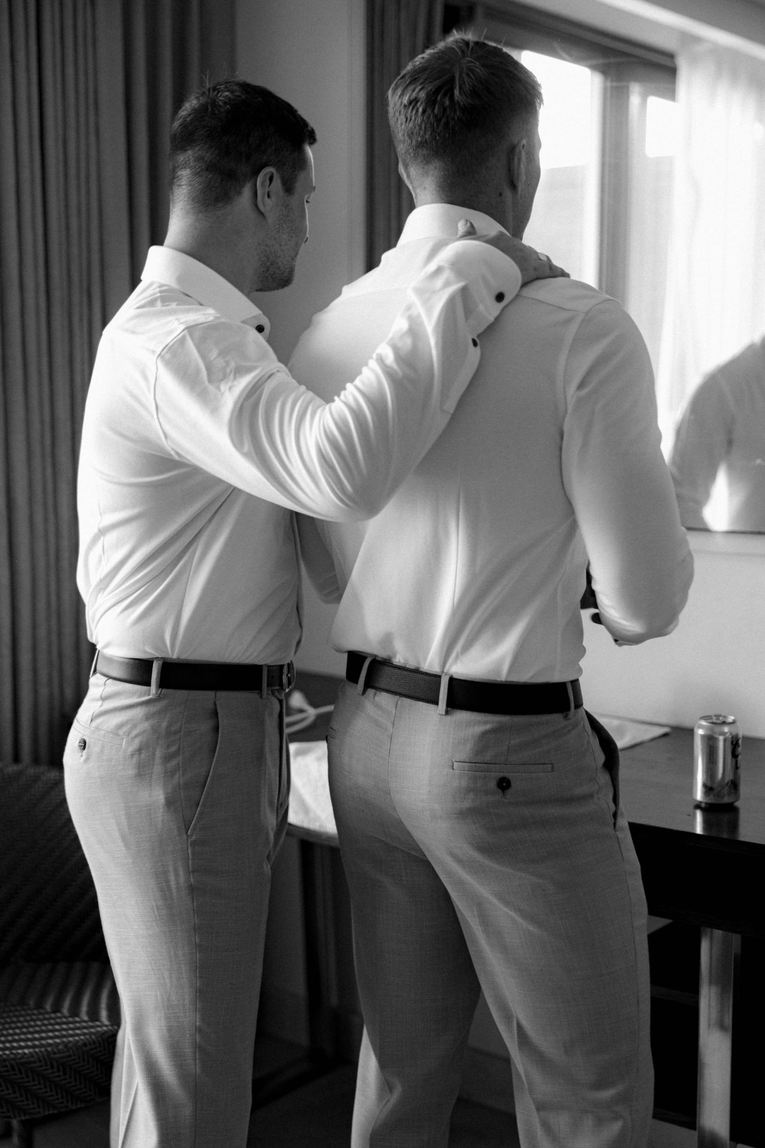 Two people in white shirts and khaki pants helping each other get dressed.
