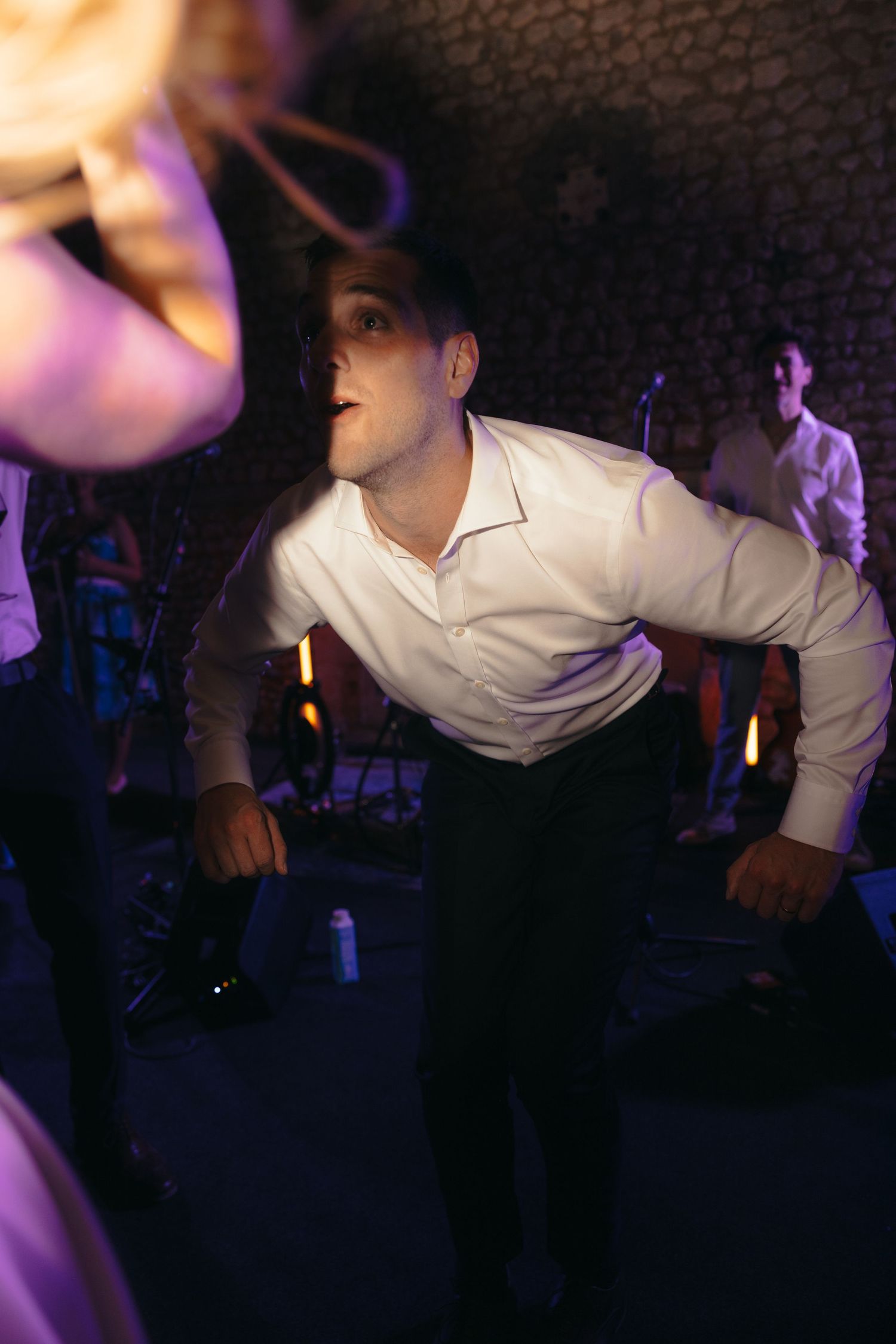 Energetic dancing at a wedding reception with purple mood lighting and brick walls.