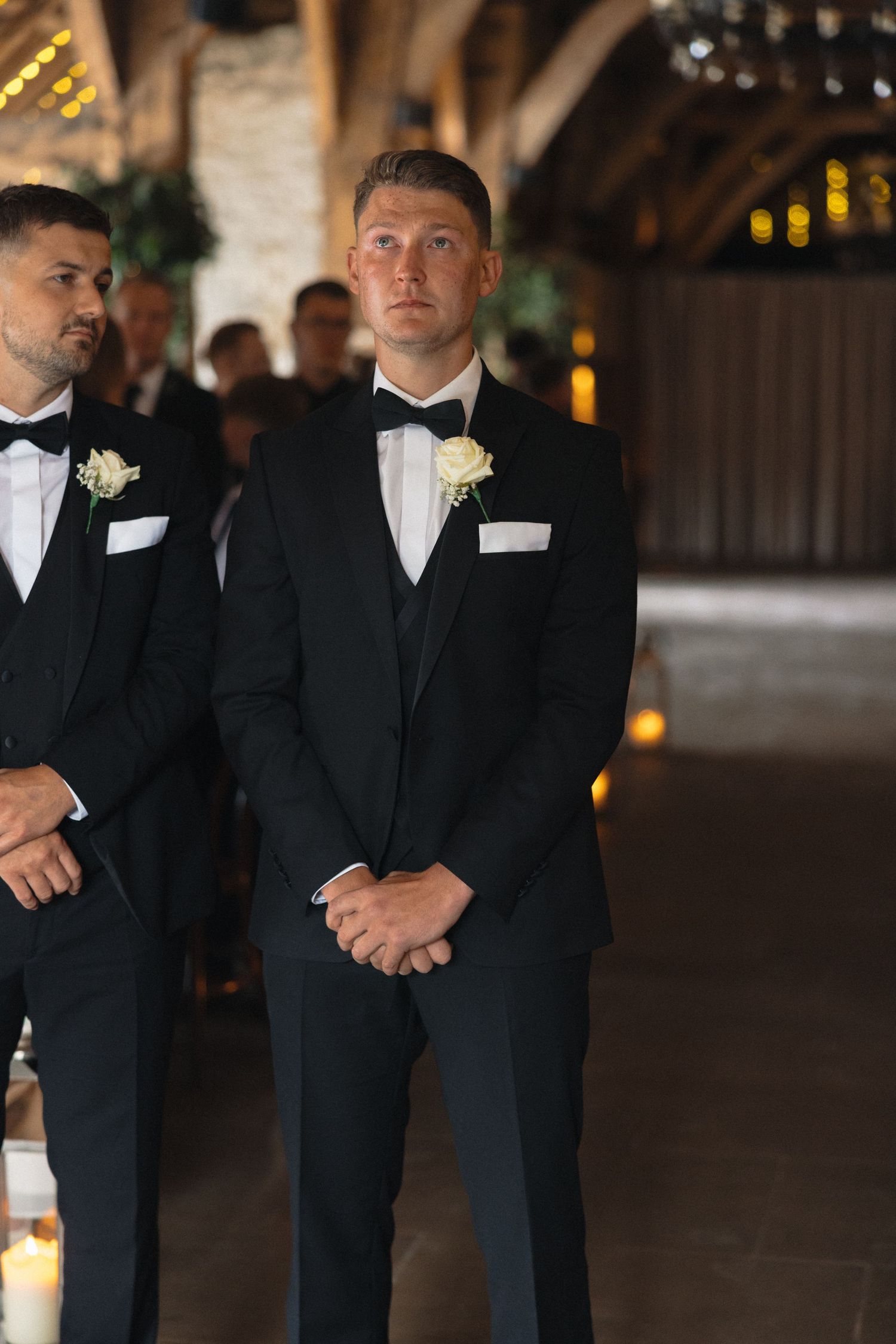 Groomsmen in formal black suits and bowties await during wedding ceremony.