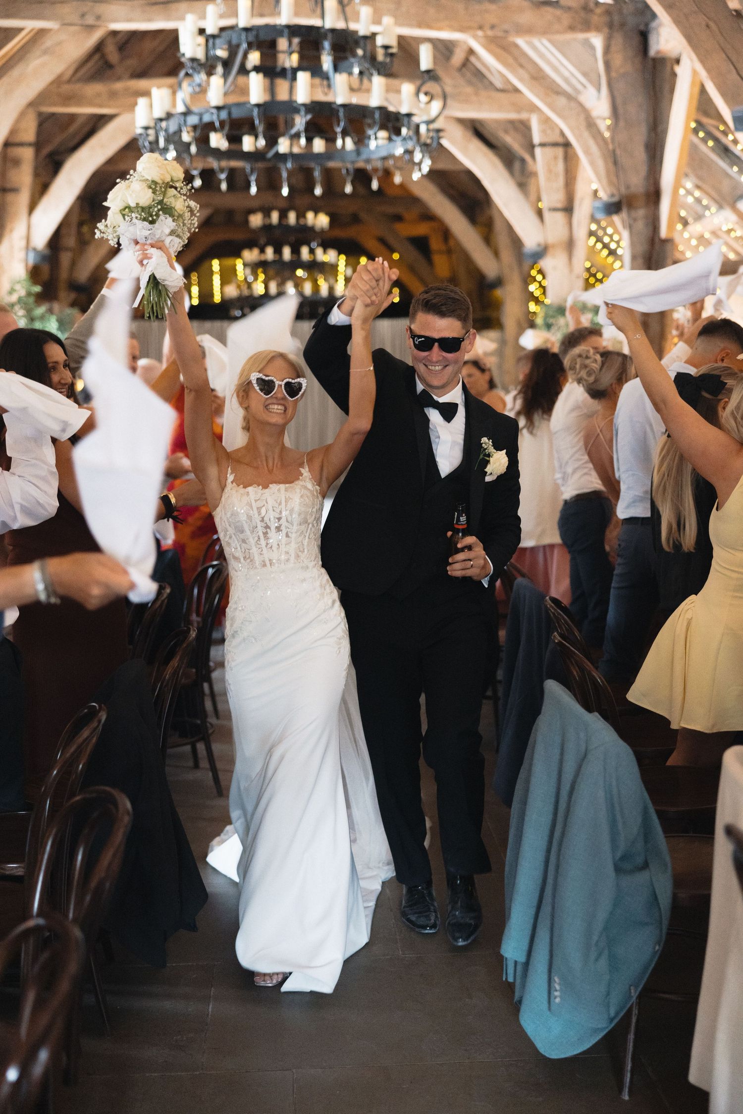 Wedding guests dancing and celebrating at a rustic venue with stone walls and chandeliers.