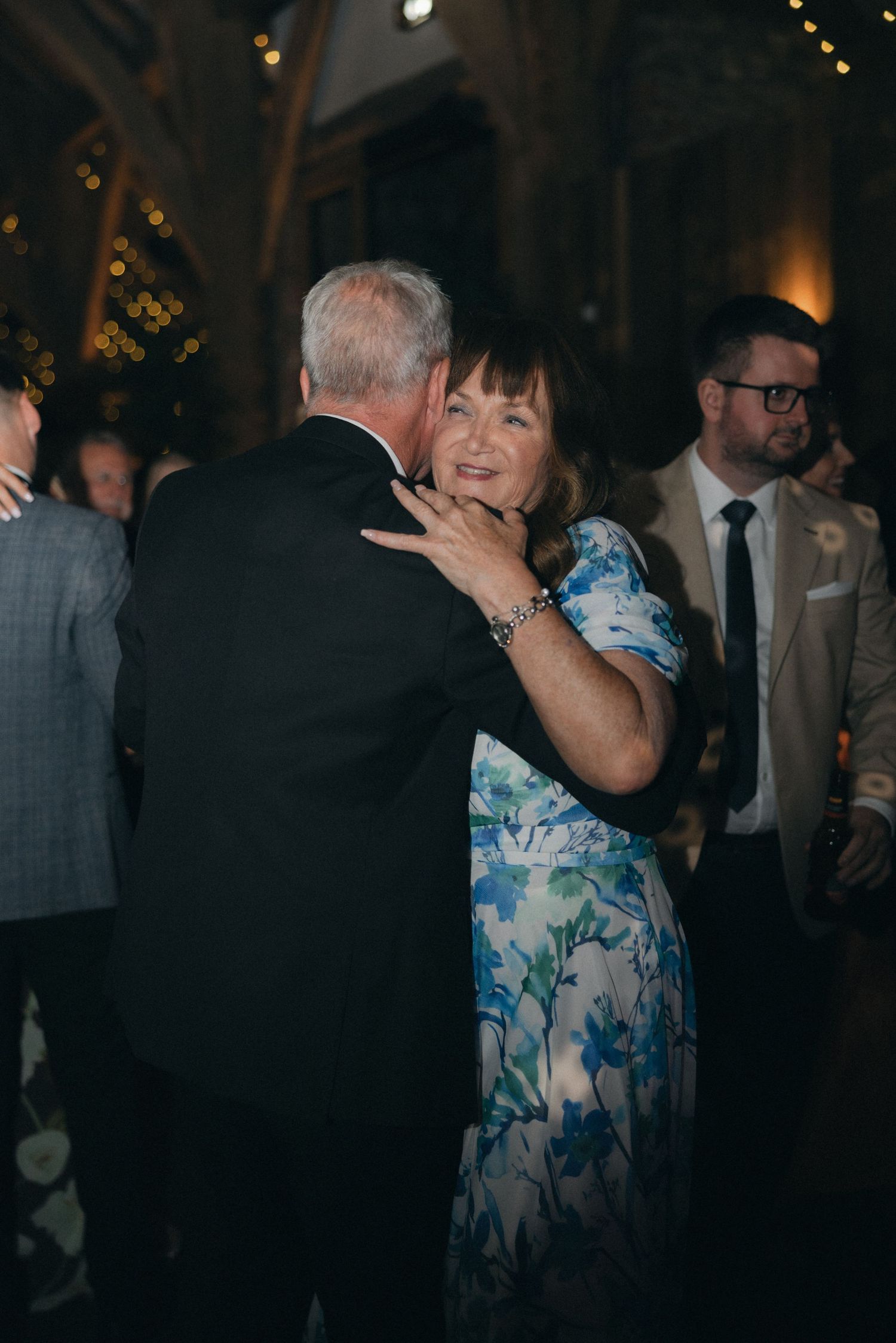 Wedding guests dance together at an evening reception with string lights overhead.
