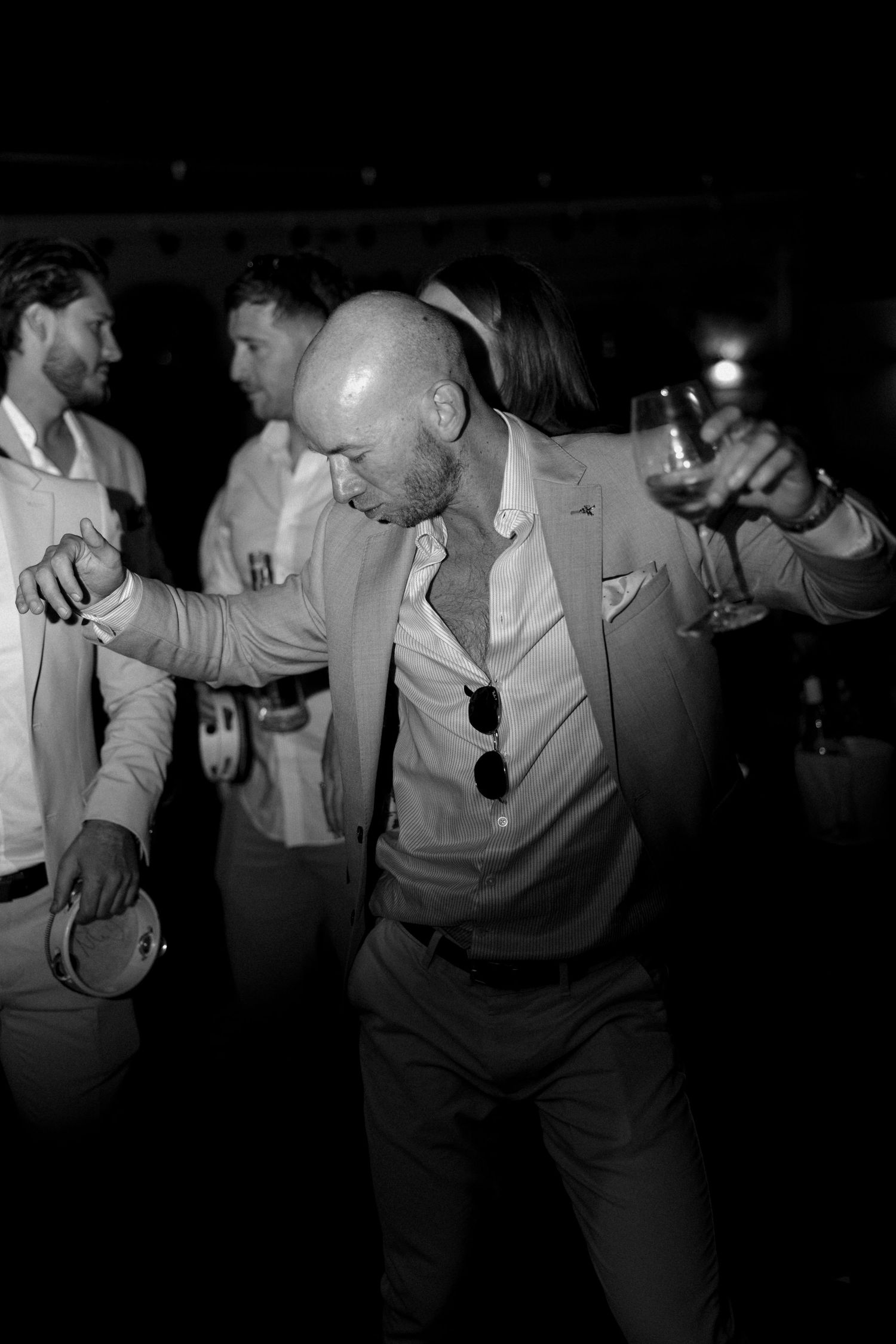 Groomsmen in light colored suits dancing at a dimly lit reception.