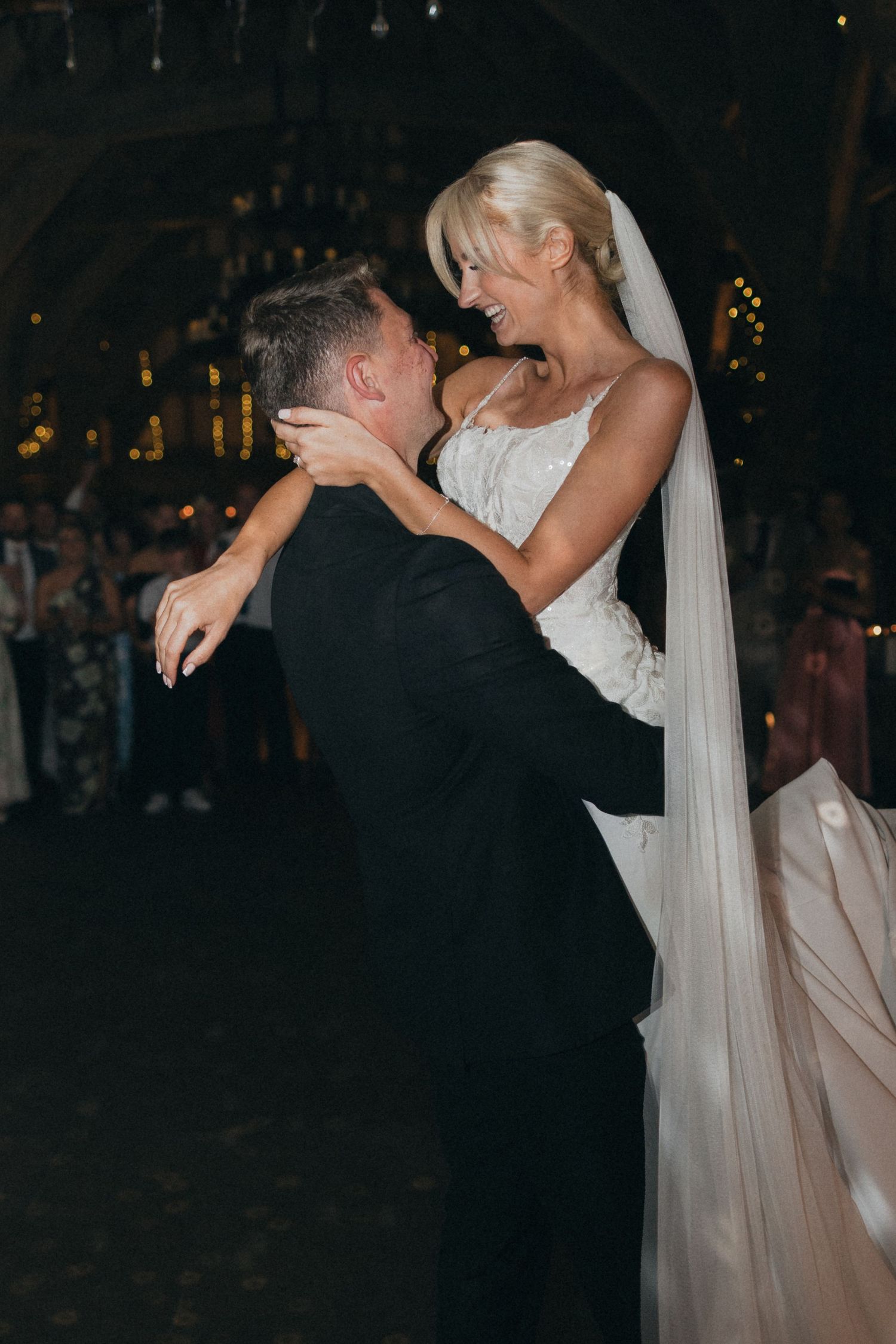 A bride in a flowing white dress and veil dances closely with her groom during their wedding reception.